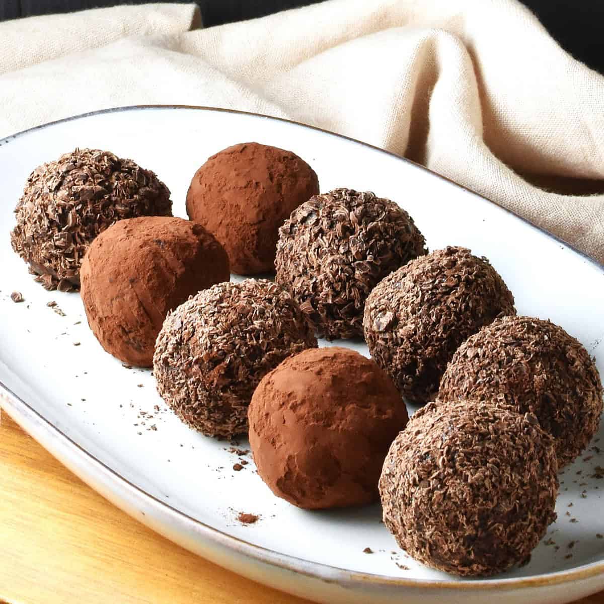 Side view of quinoa energy balls coated in cocoa and chocolate flakes on white oval plate.