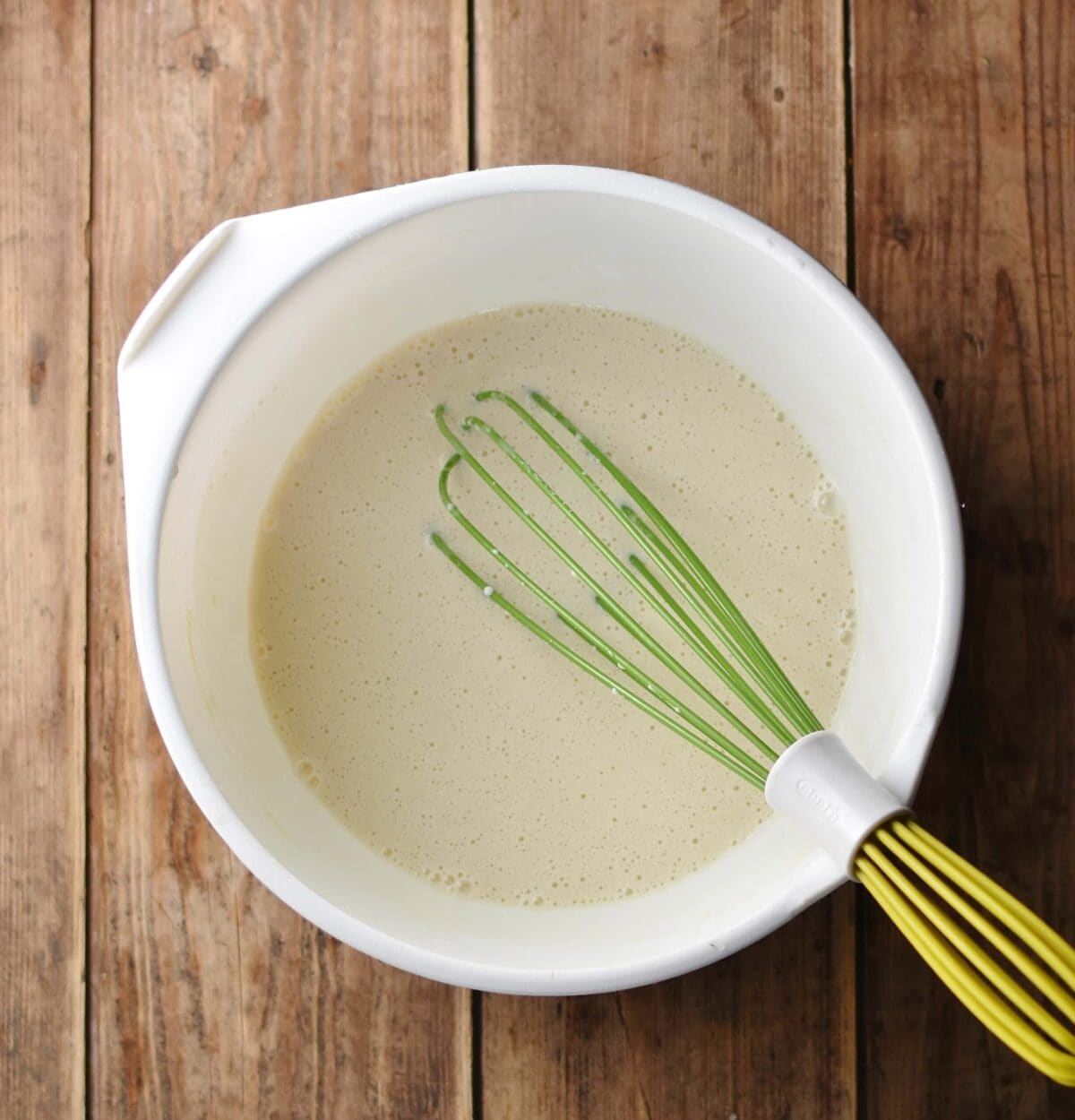 Crepes batter in large white bowl with green whisk.