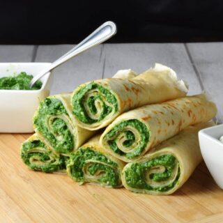 Crepes with spinach filling on light wooden board with white dish with spinach mixture and spoon in background.