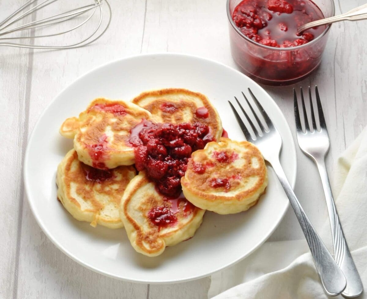 Polish pancakes on white plate with raspberry compote and forks on white table.