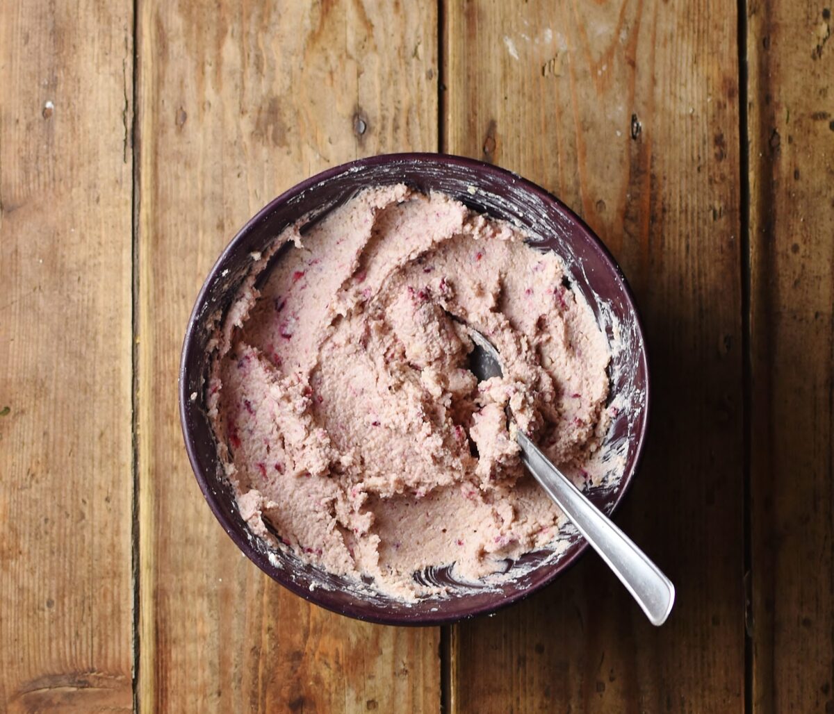 Creamy strawberry cheese mixture with spoon in purple bowl.