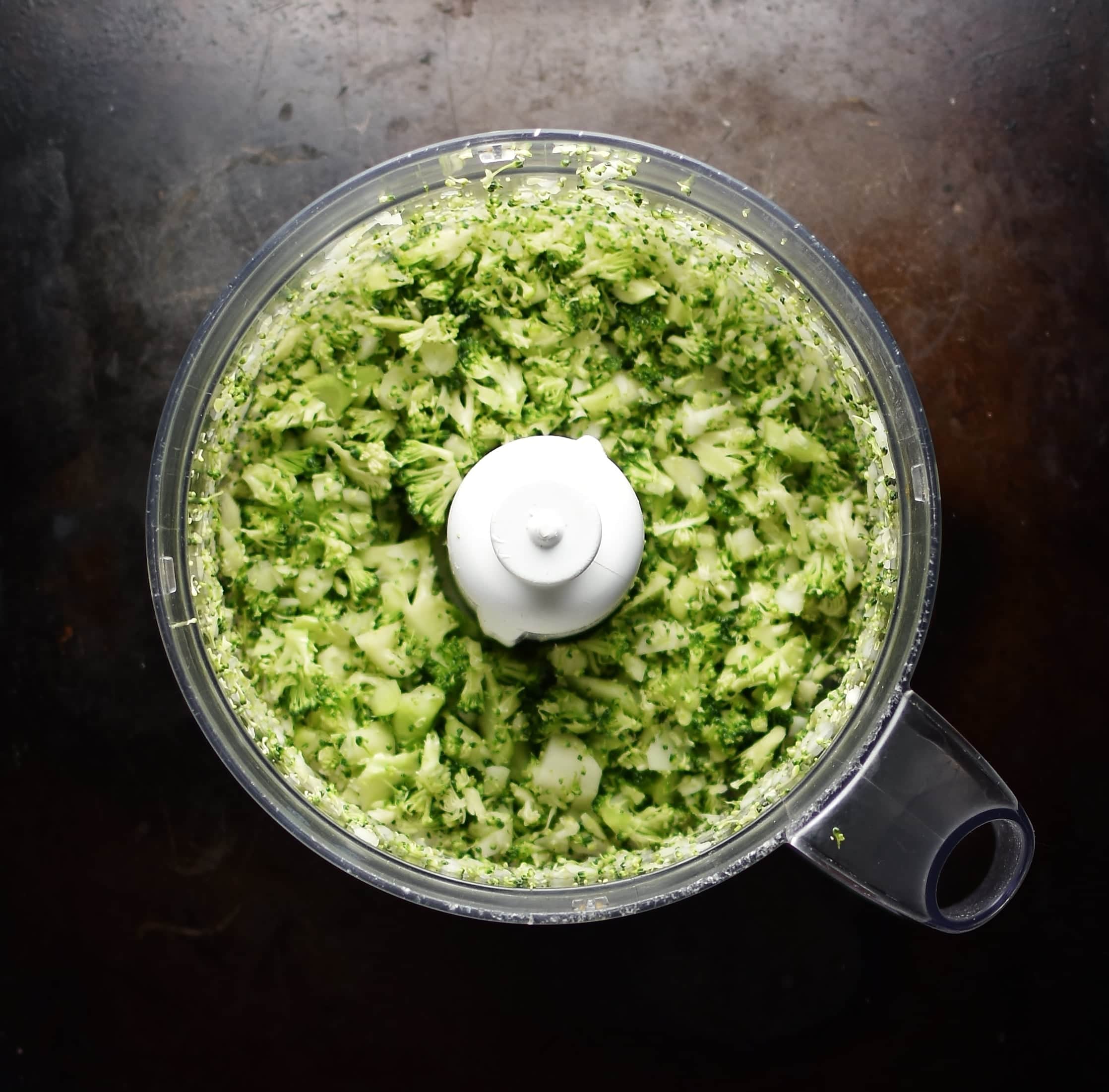 Top down view of broccoli rice in blender on dark surface.