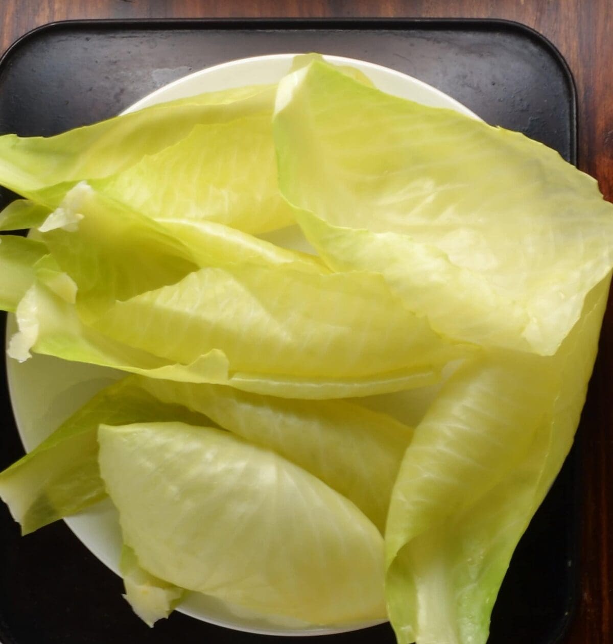 Cooked loose cabbage leaves on white plate on dark surface.