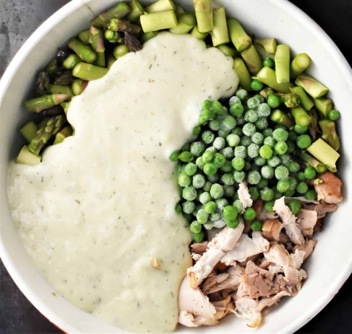 Chopped chicken, asparagus, peas and creamy sauce in large bowl.