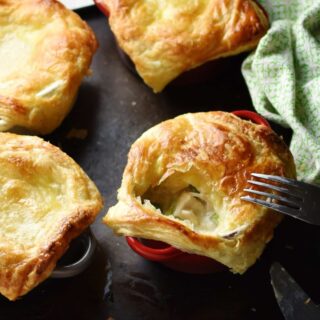 Close-up view of mini chicken pies with fork and green cloth to right on top of dark tray.
