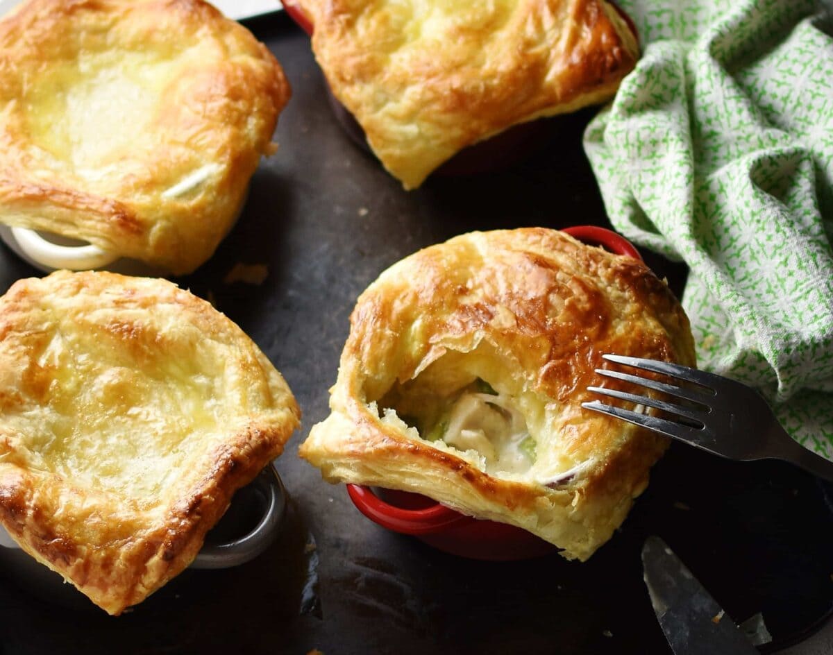 Close-up view of mini chicken pies with fork and green cloth to right on top of dark tray.