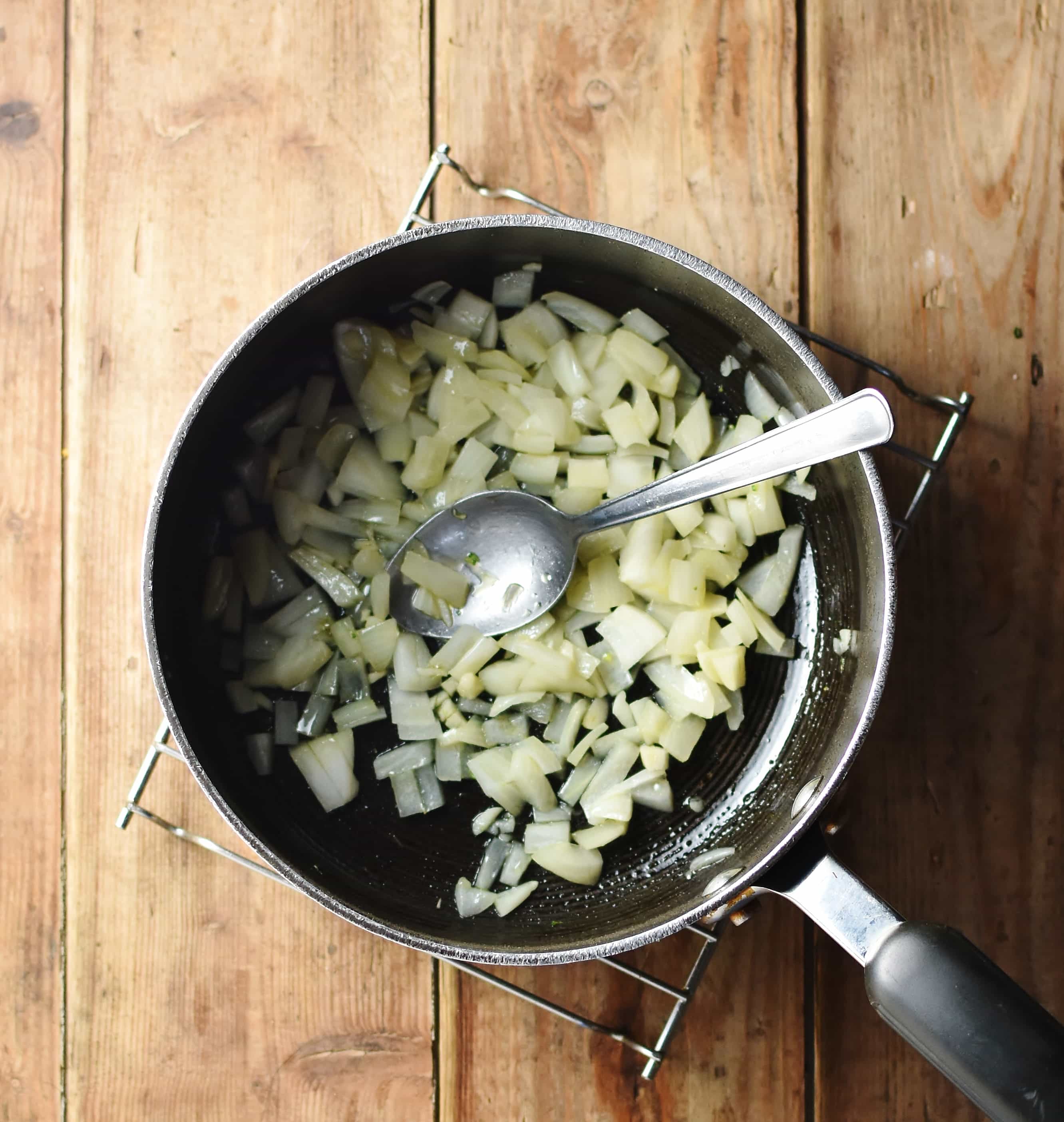 Chopped onions in large pot with spoon.