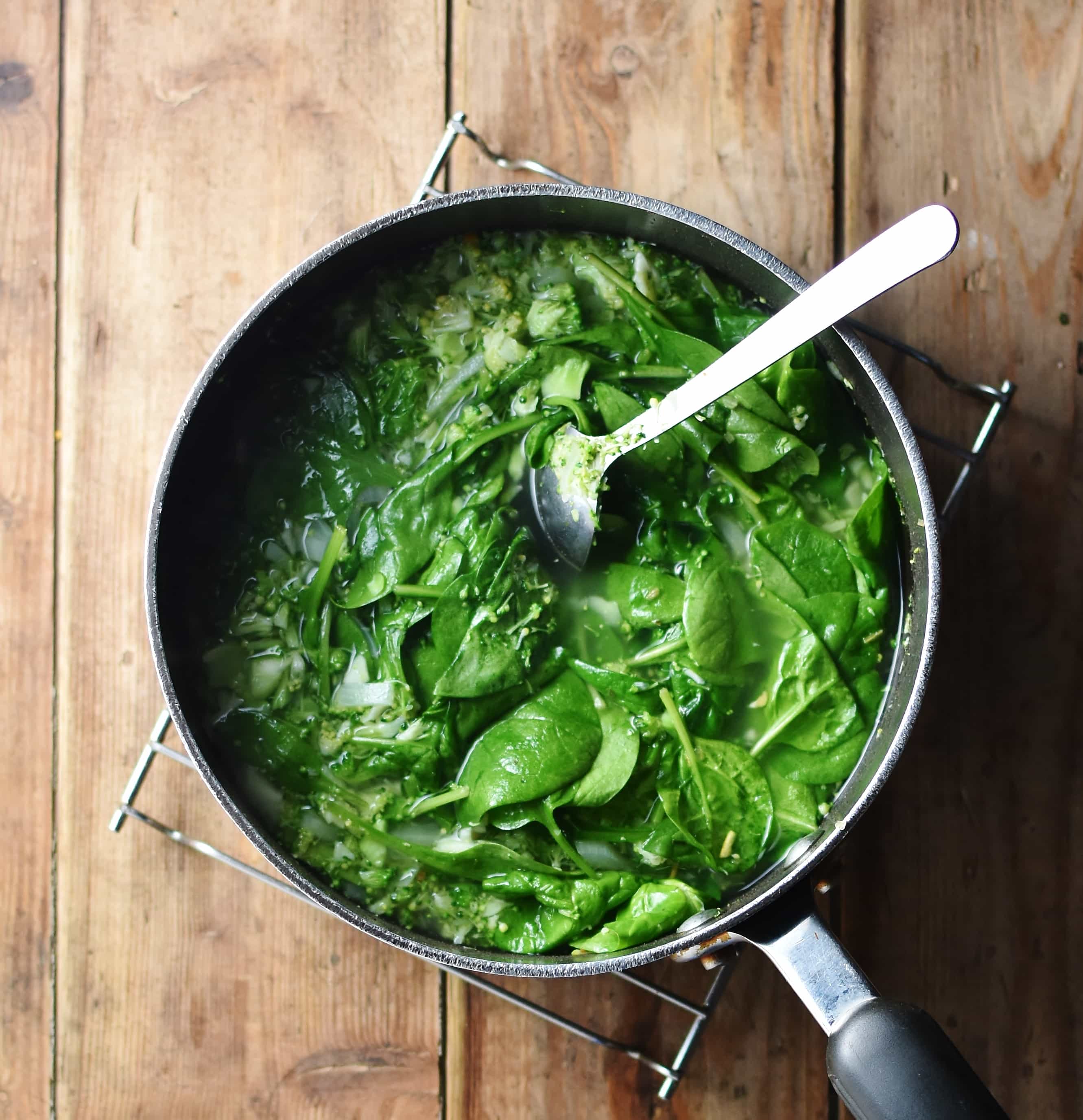 Spinach with water in large pot with spoon.