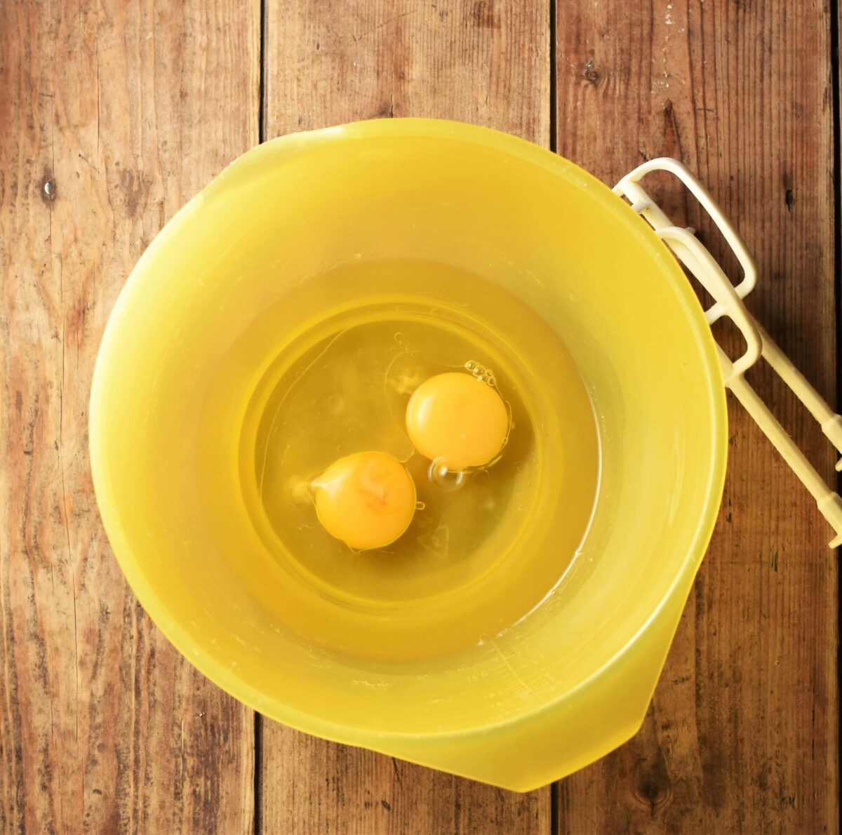 2 eggs and oil in large yellow bowl with electric mixer end pieces.