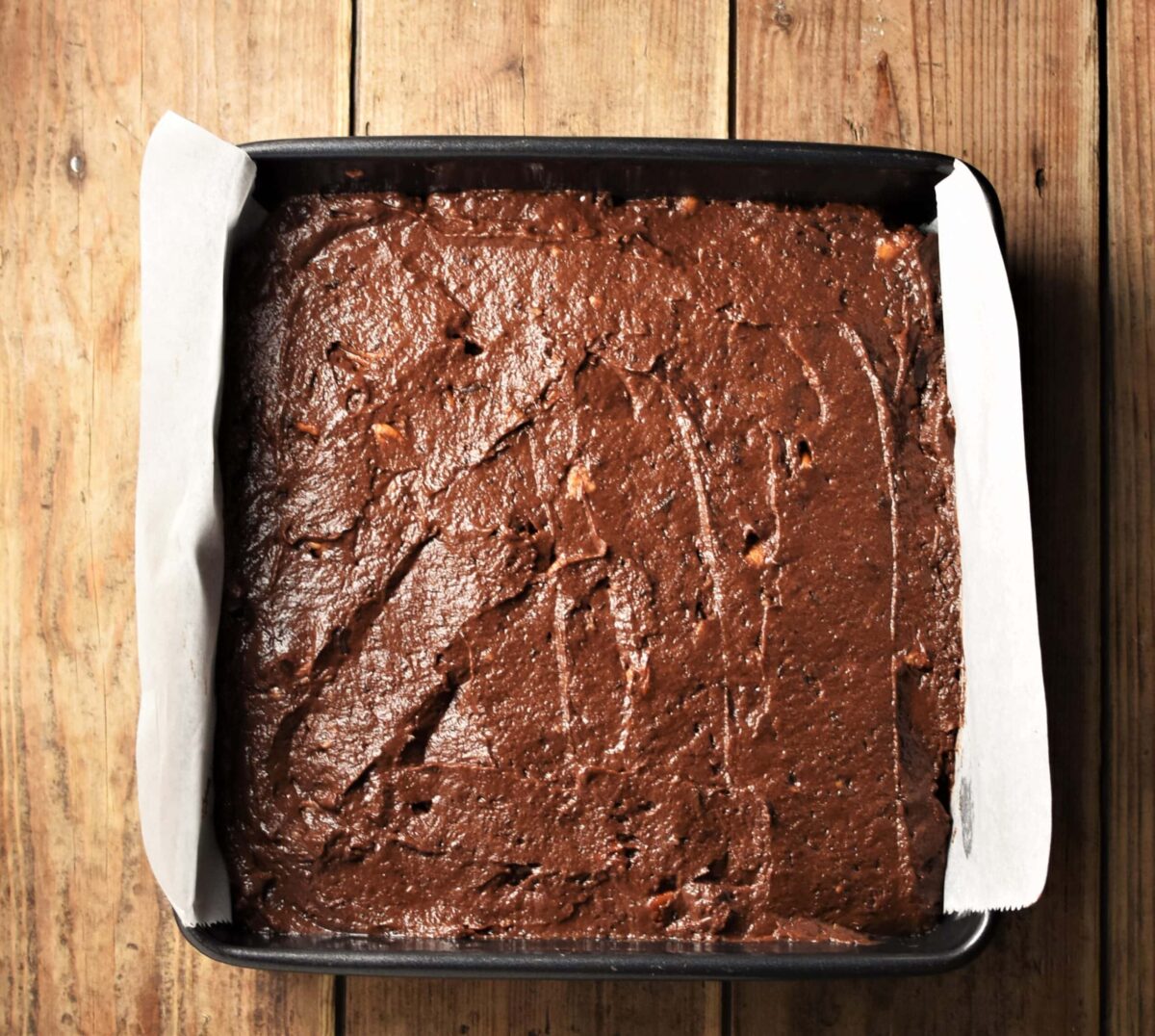 Brownie cake batter in square pan lined with parchment paper.