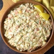 Top down view of creamy salmon egg salad with lemon wedges in brown bowl.