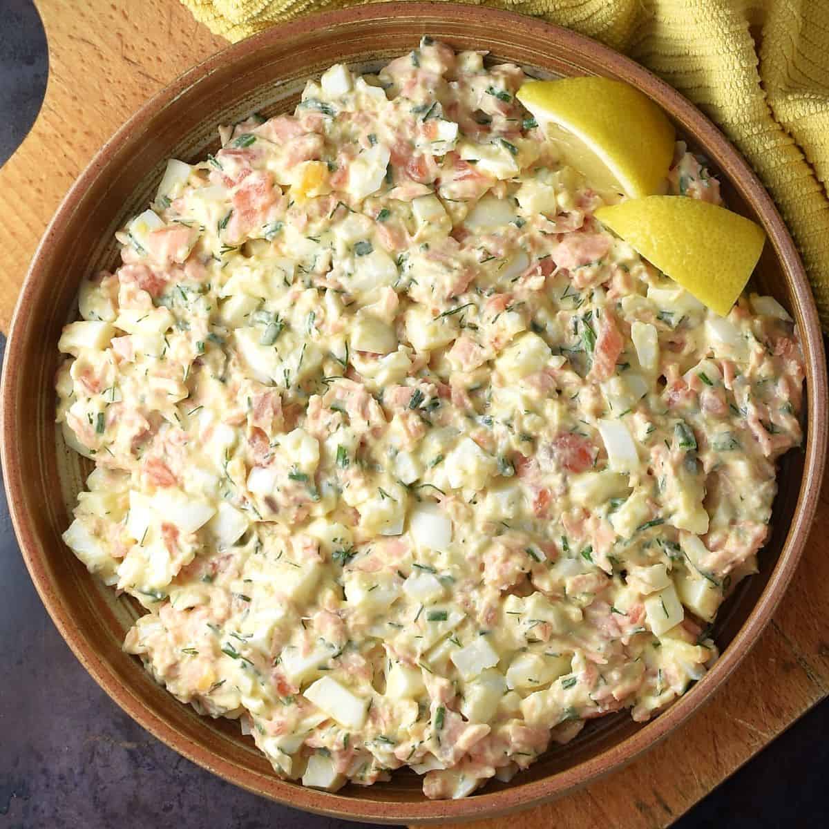 Top down view of creamy salmon egg salad with lemon wedges in brown bowl.