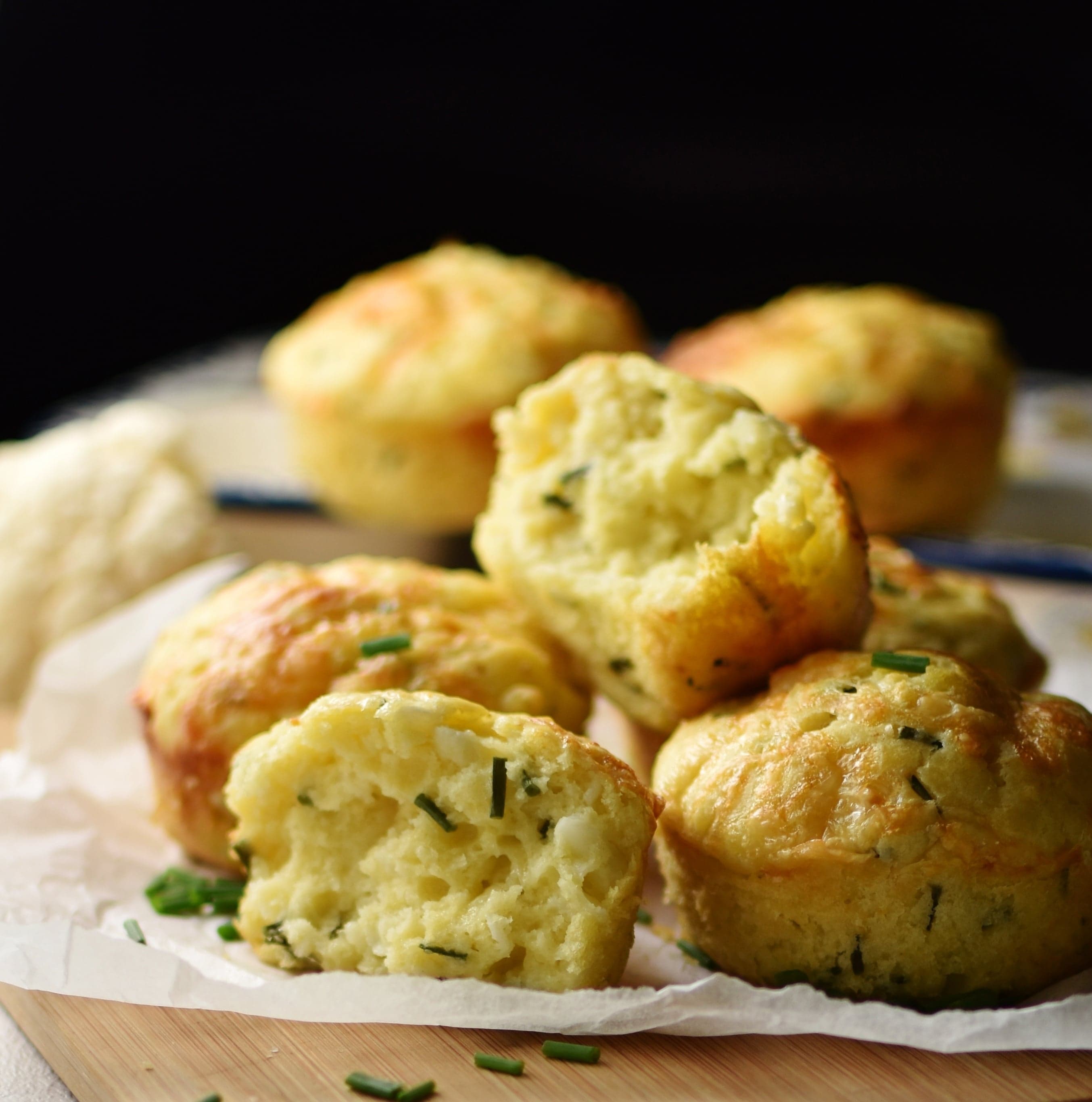 Side view of cauliflower muffins on top of wooden board lined with baking paper.