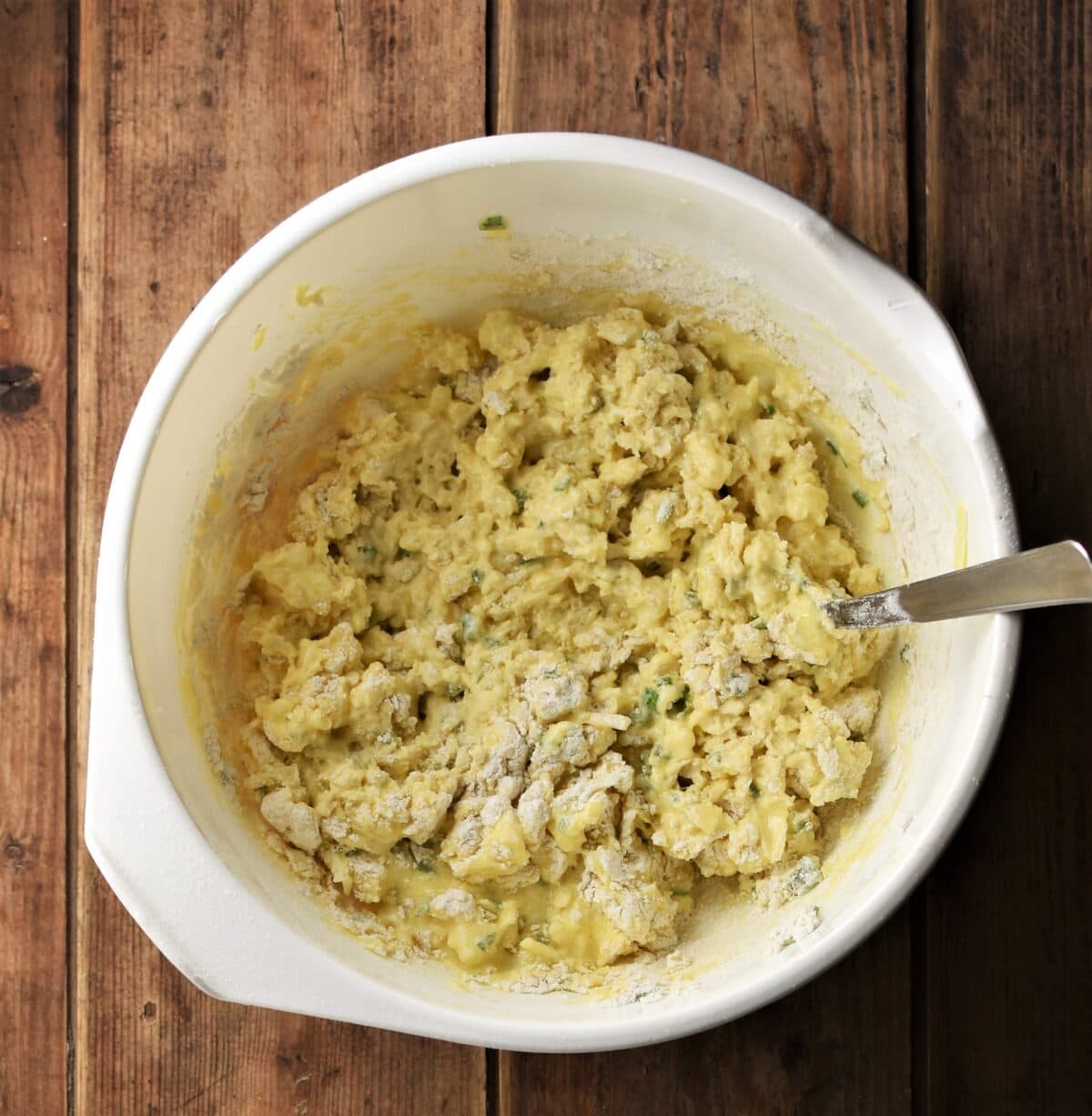 Lumpy cauliflower muffin batter in large white bowl with spoon.