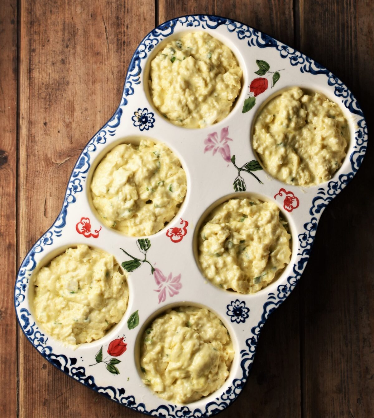 Lumpy batter in 6-hole white ceramic muffin pan with flowery blue pattern.