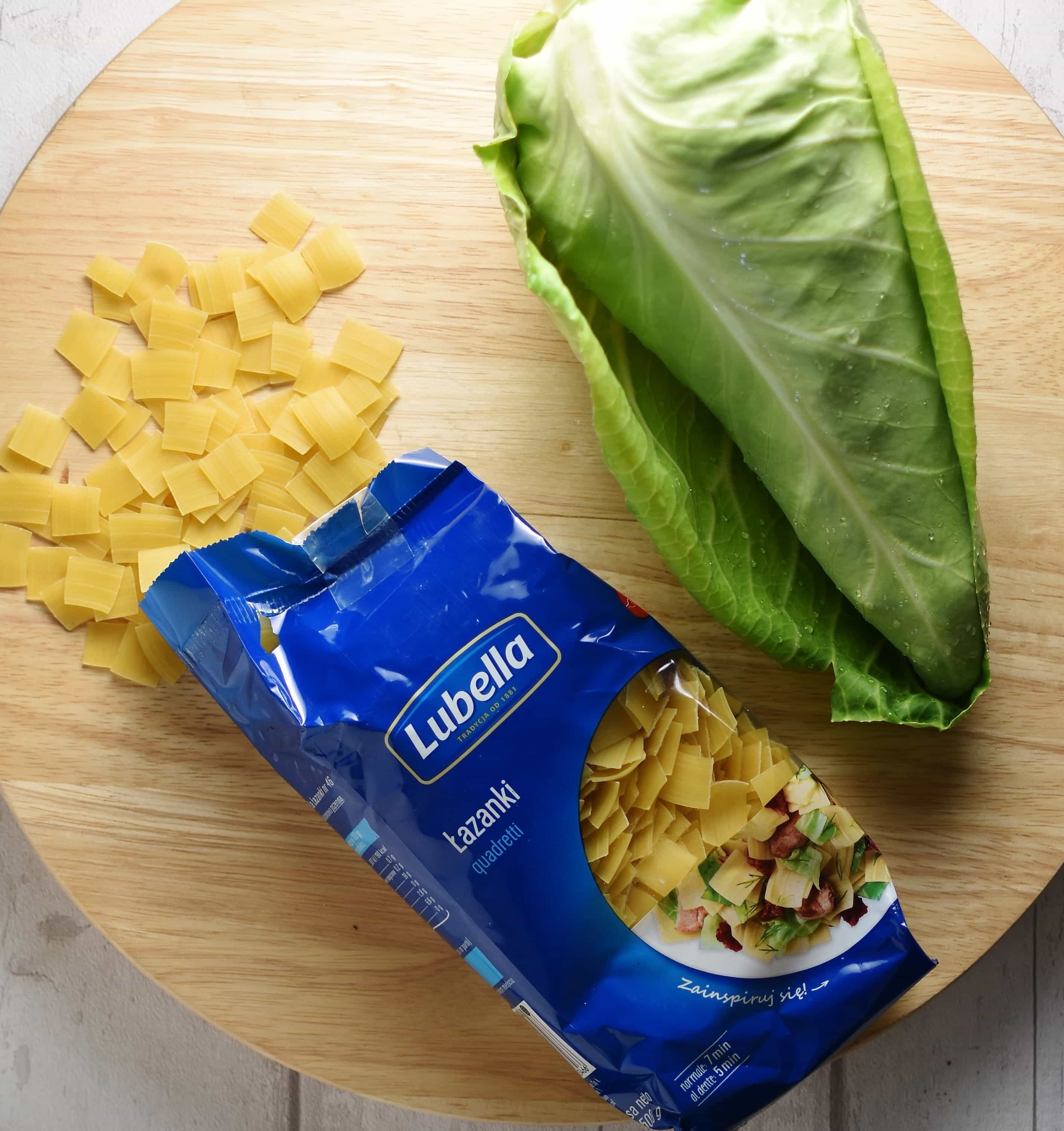 Top down view of Polish lazanki pasta in package, with pointed cabbage on top of round wooden board.