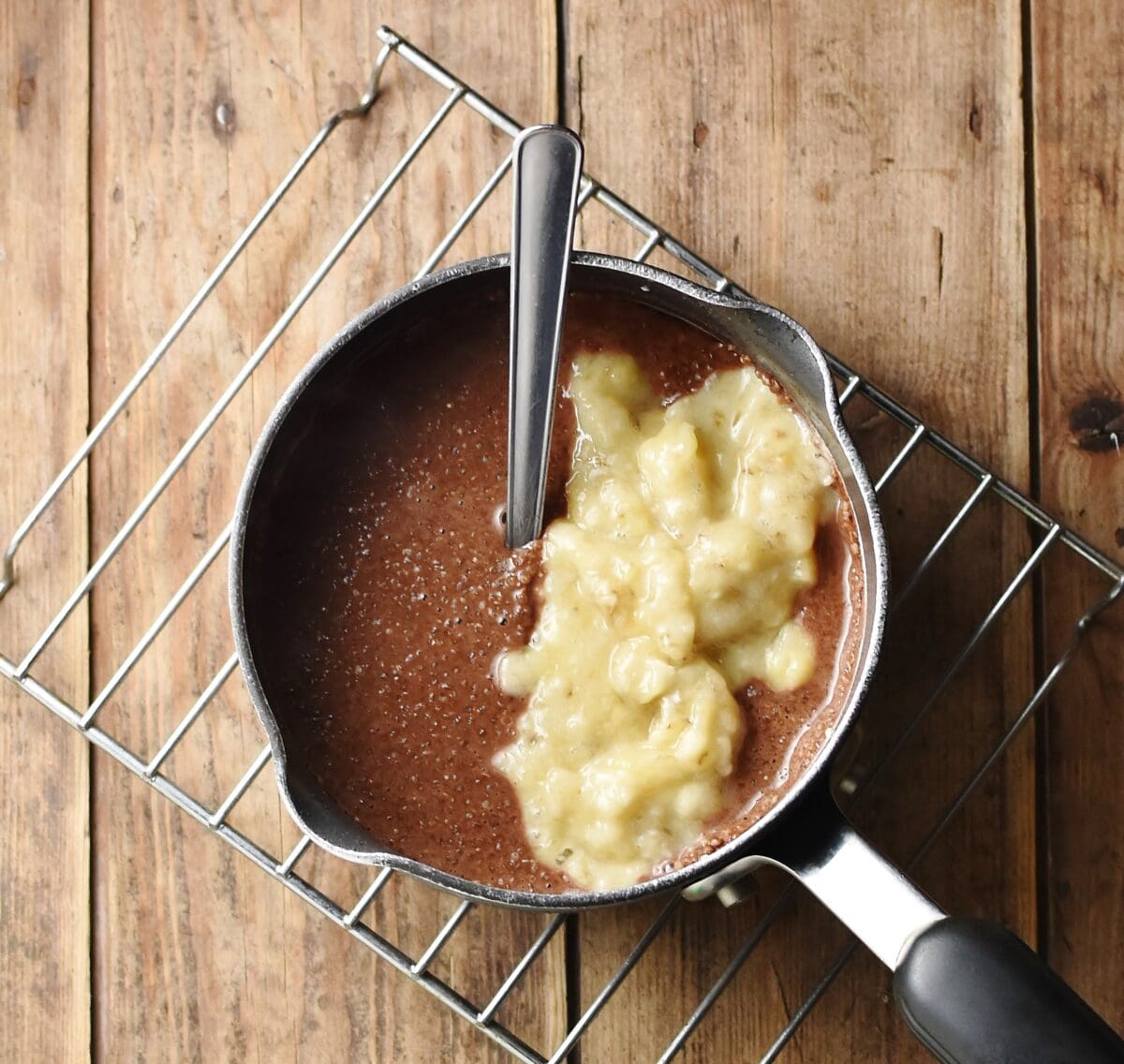 Chocolate quinoa porridge with mashed banana in saucepan with spoon.