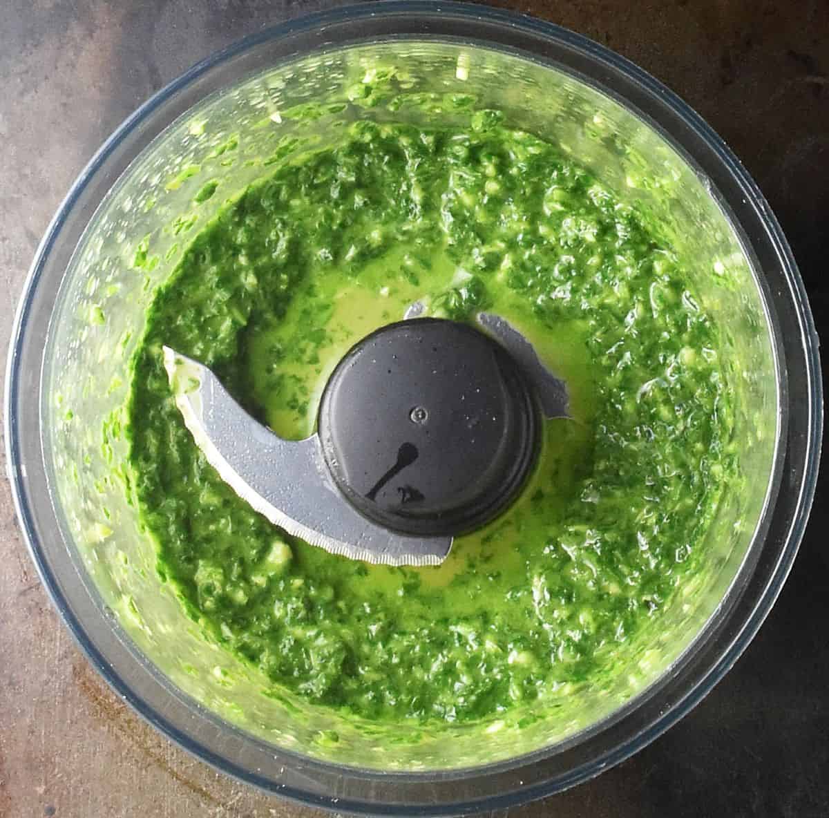 Top down view of blended fresh basil in food processor bowl.