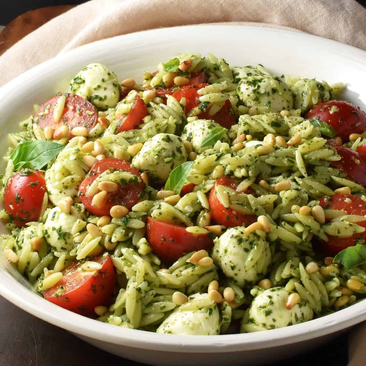 Side view of orzo pesto salad with mini mozzarellas and tomatoes in white bowl.