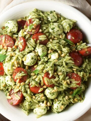 Top down view of caprese orzo salad with pesto in large white bowl with spoon.
