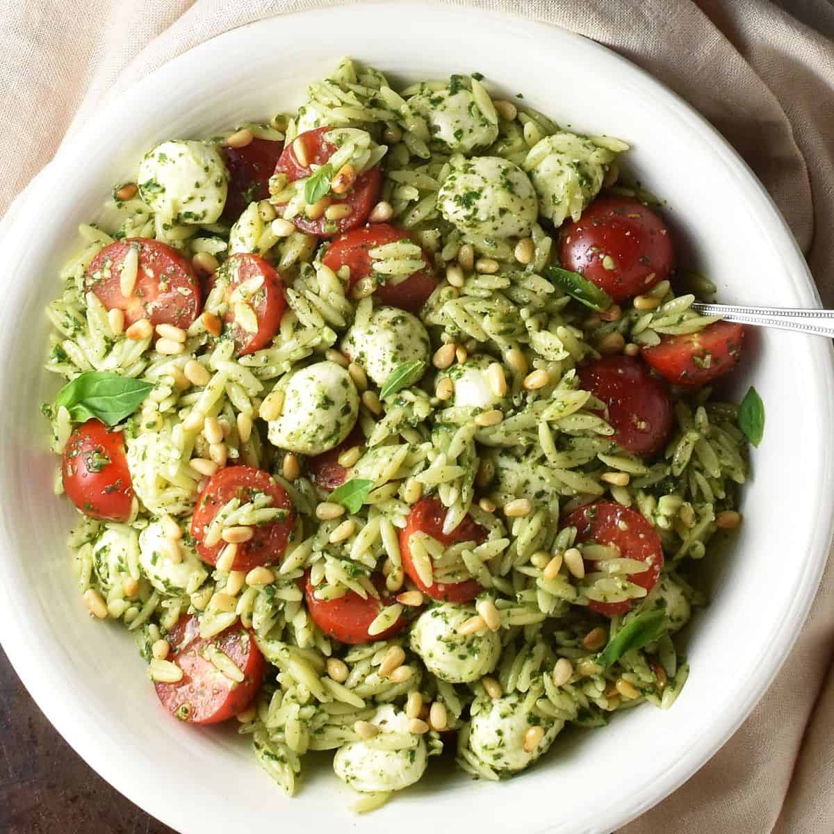 Top down view of caprese orzo salad with pesto in large white bowl with spoon.