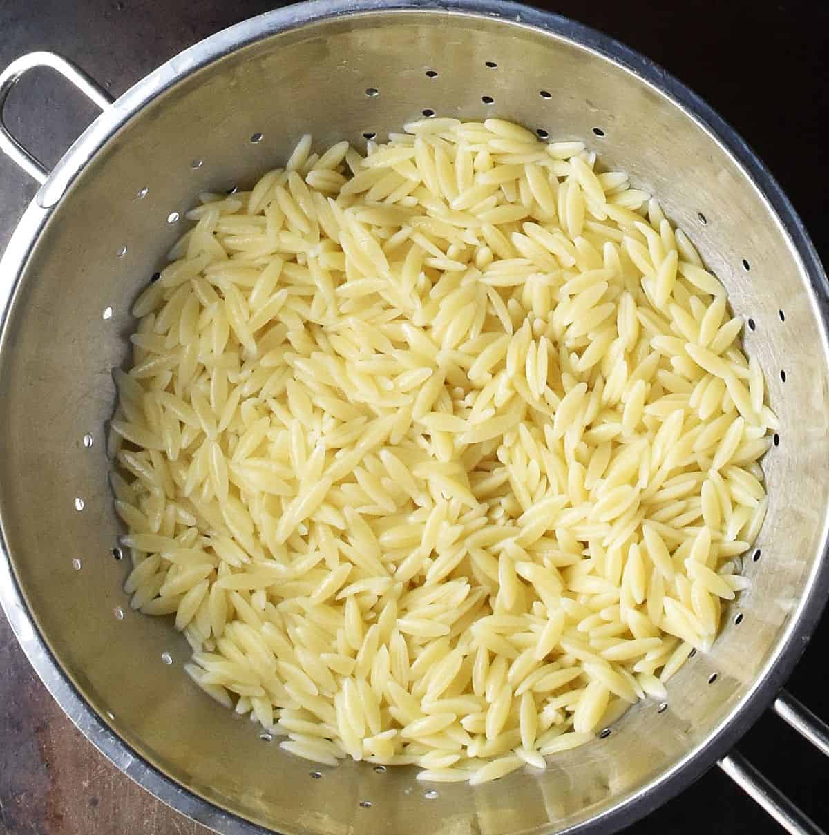 Top down view of cooked orzo pasta in colander.