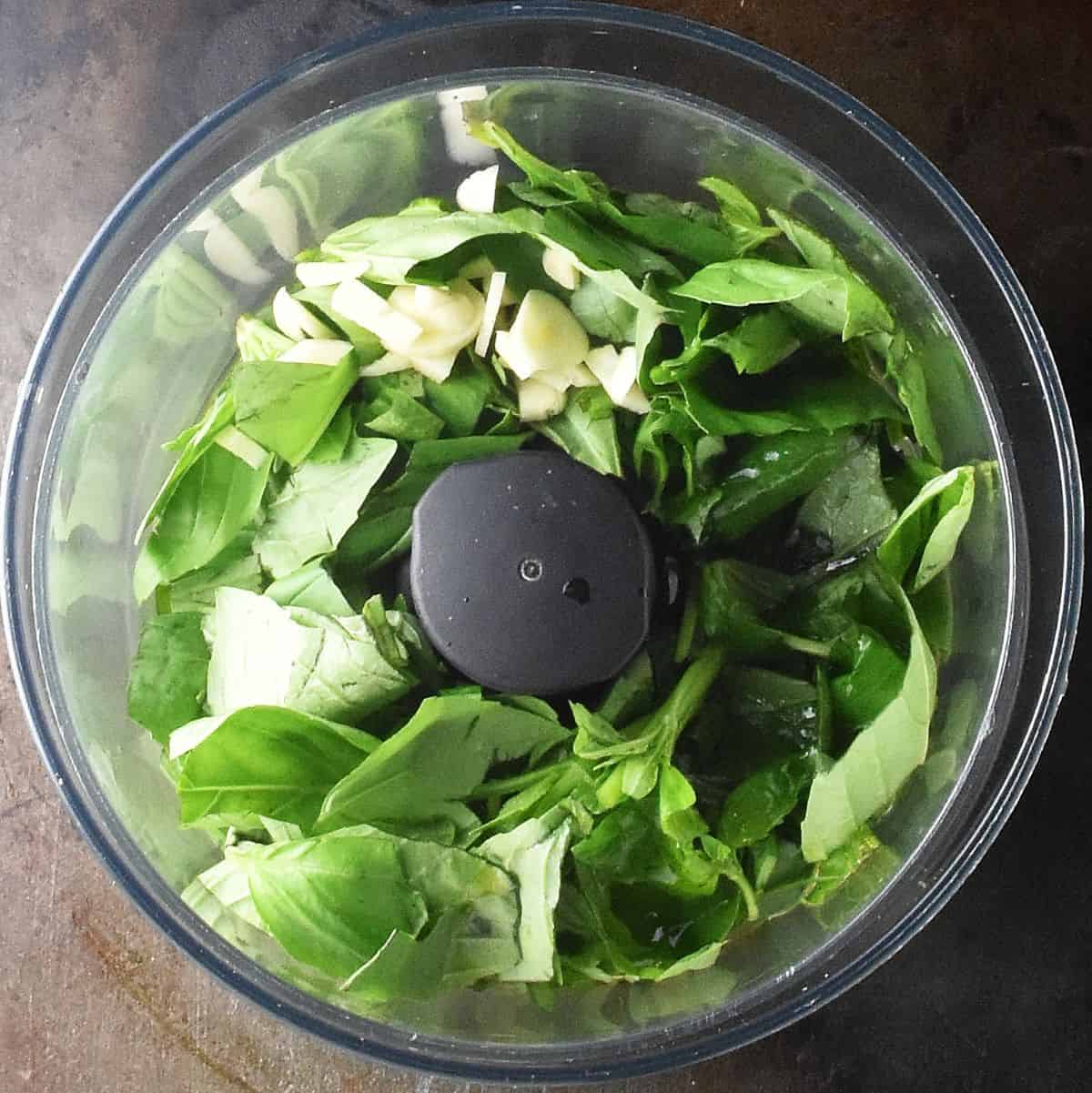 Fresh basil and chopped garlic in food processor bowl.