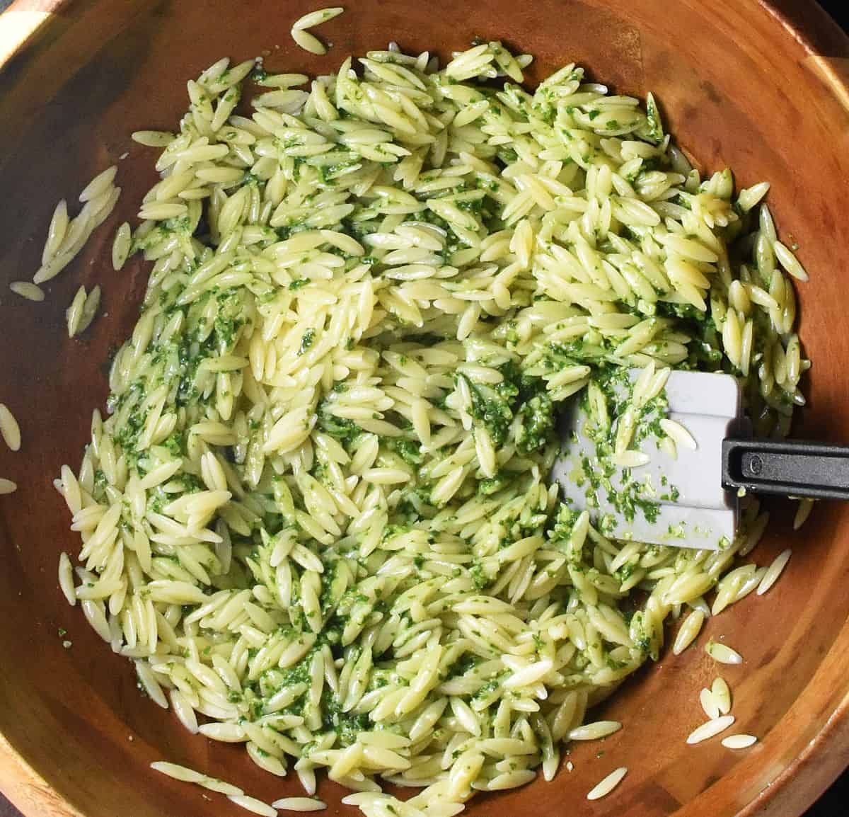 Orzo pasta with pesto sauce in large wooden bowl with grey spatula.