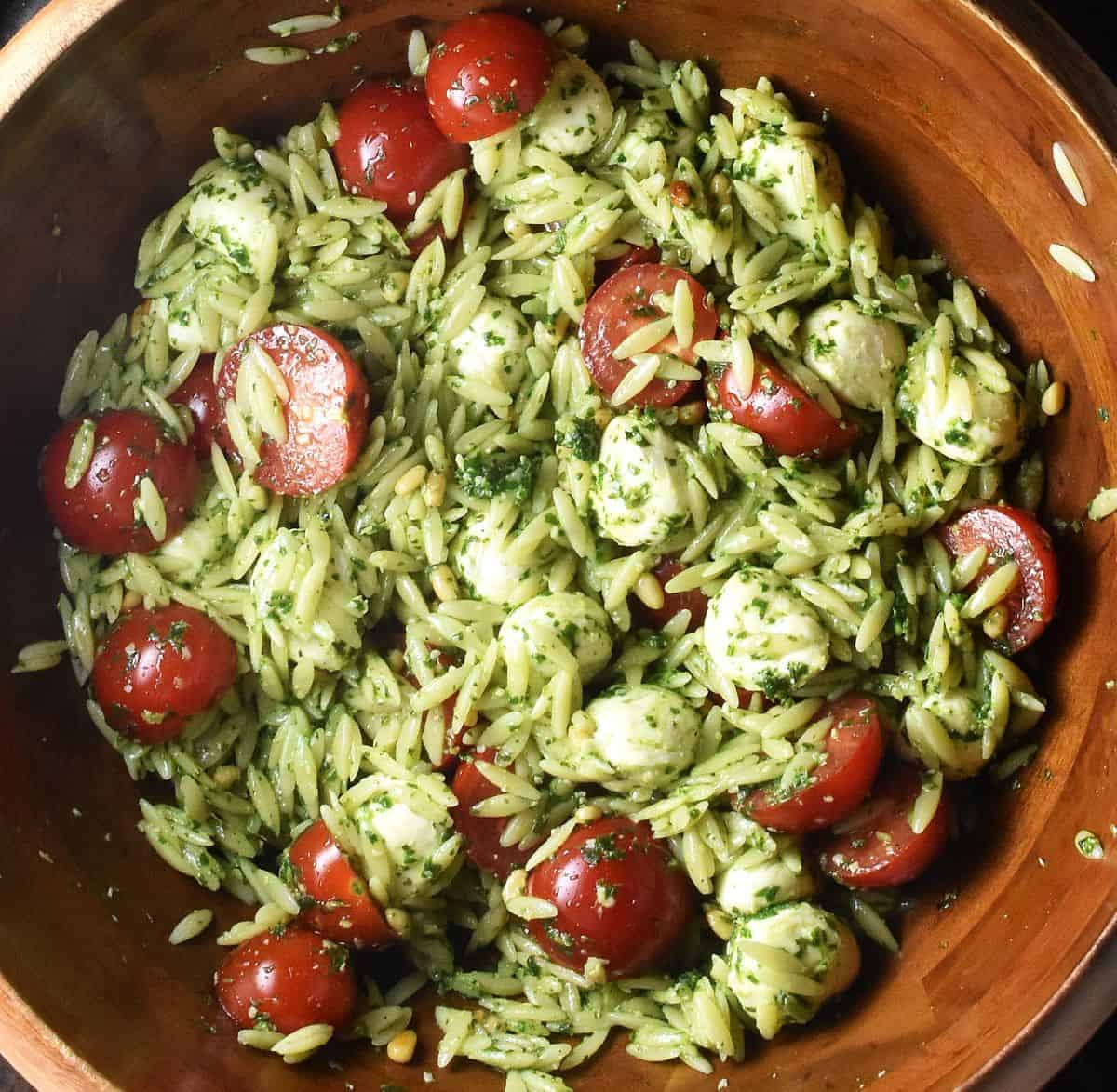 Top down view of pesto pasta salad with mozzarella pearls and mini tomatoes in wooden bowl.