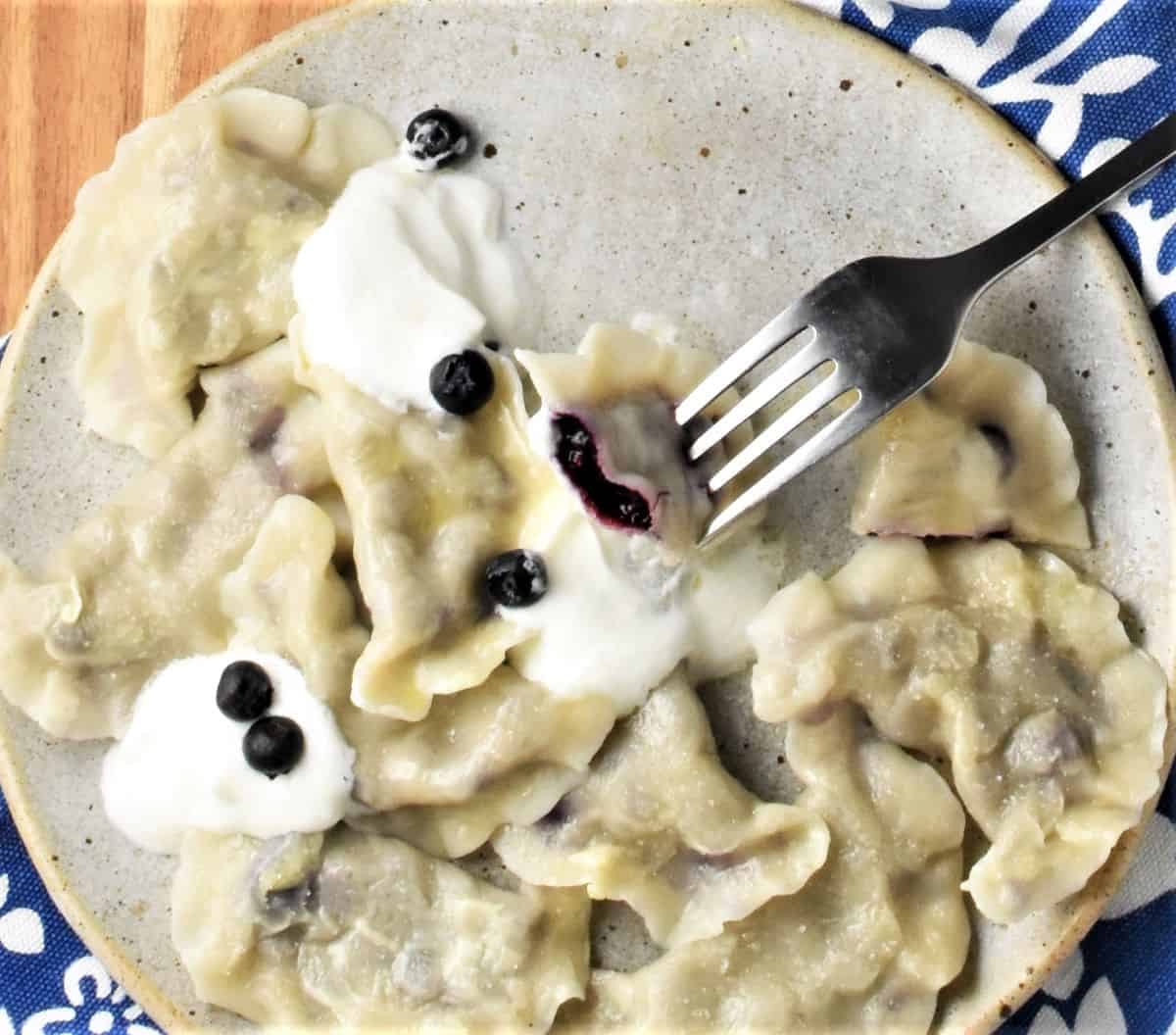 Plate of blueberry pierogi with one pierced with fork.