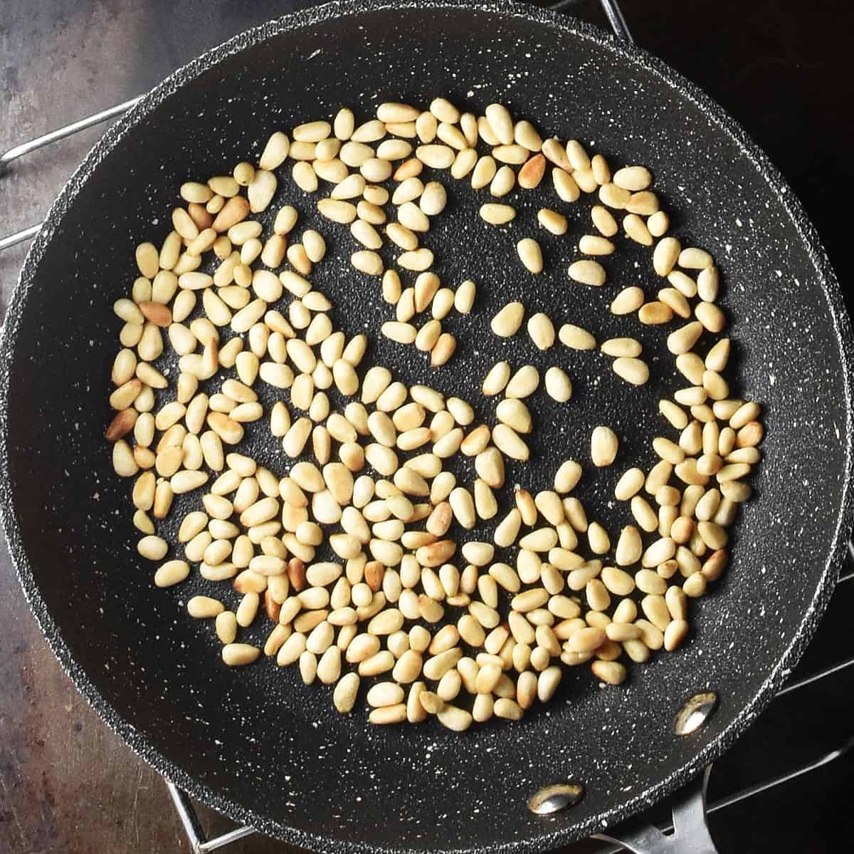 Top down view of toasted pine nuts in black pan.