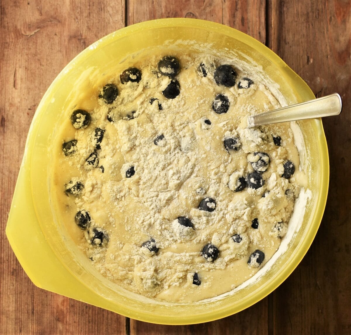 Blueberry cake batter in yellow bowl with spoon.