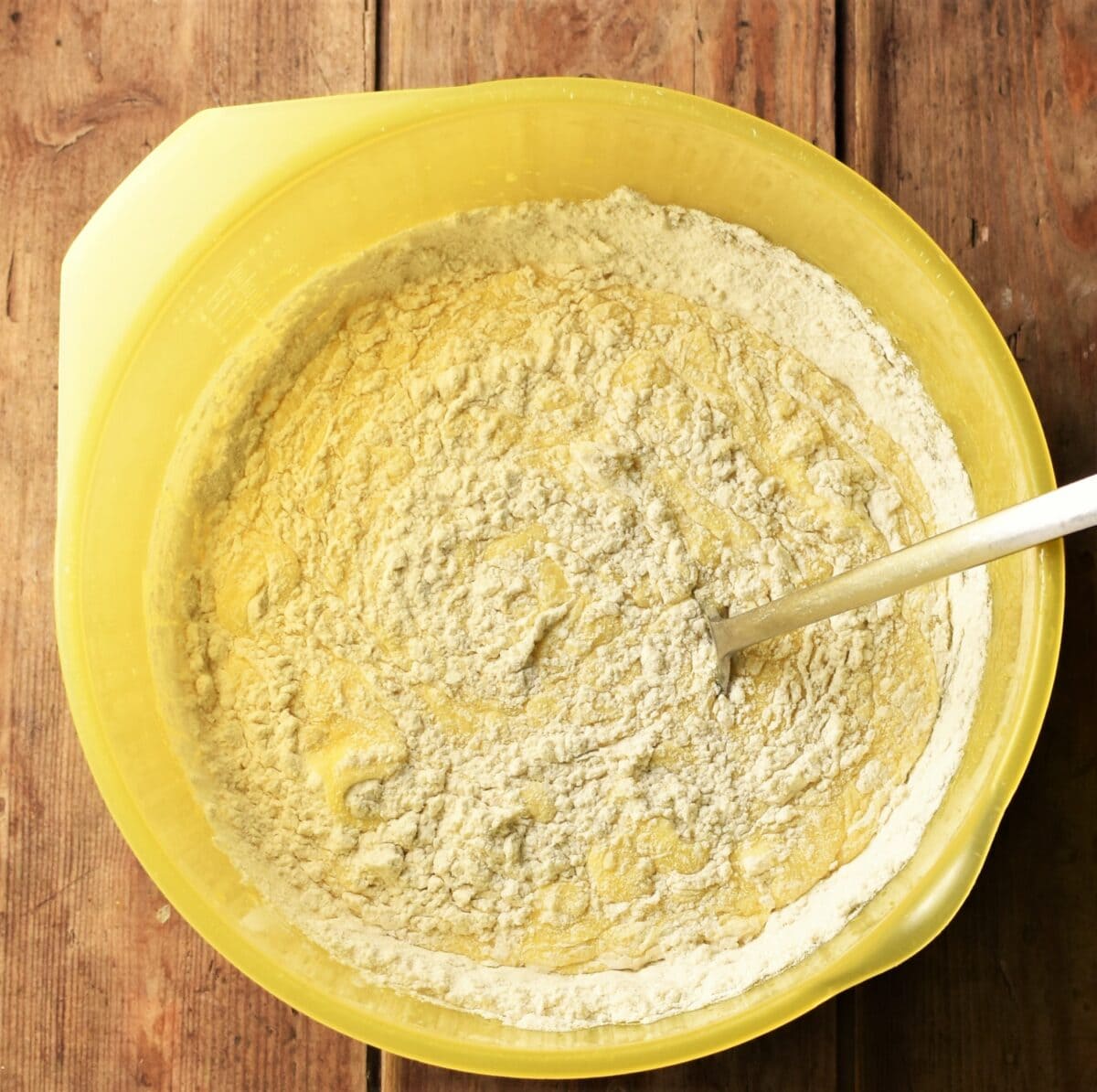 Cake batter with some flour visible in yellow bowl with spoon.