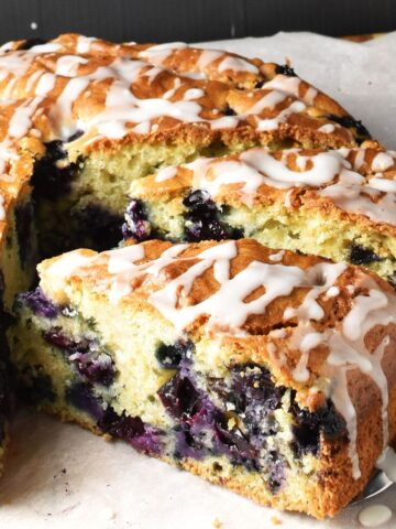 Side view of simple blueberry cake slice with cake in background on top of parchment.