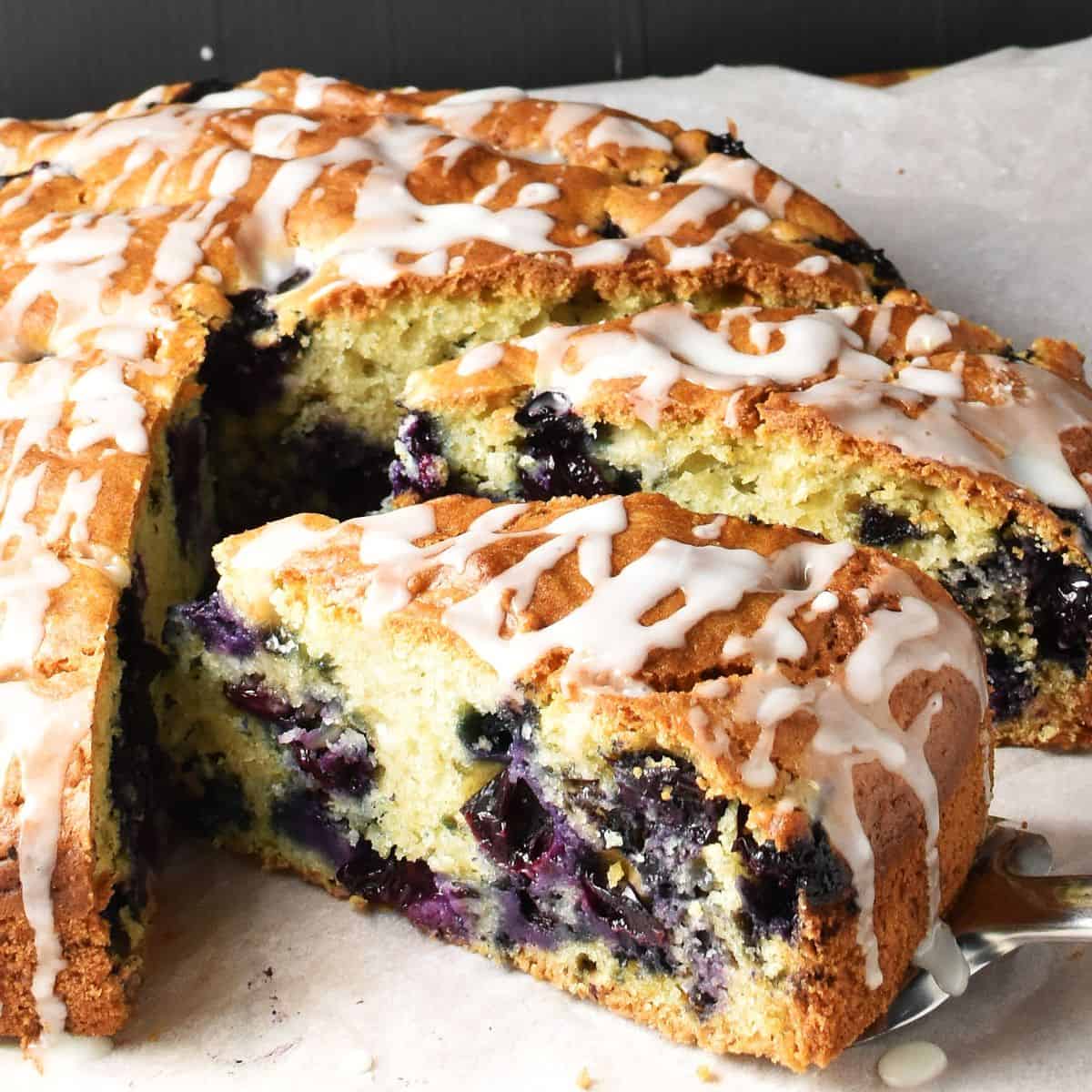Side view of blueberry muffin cake slice with cake in background on top of parchment.