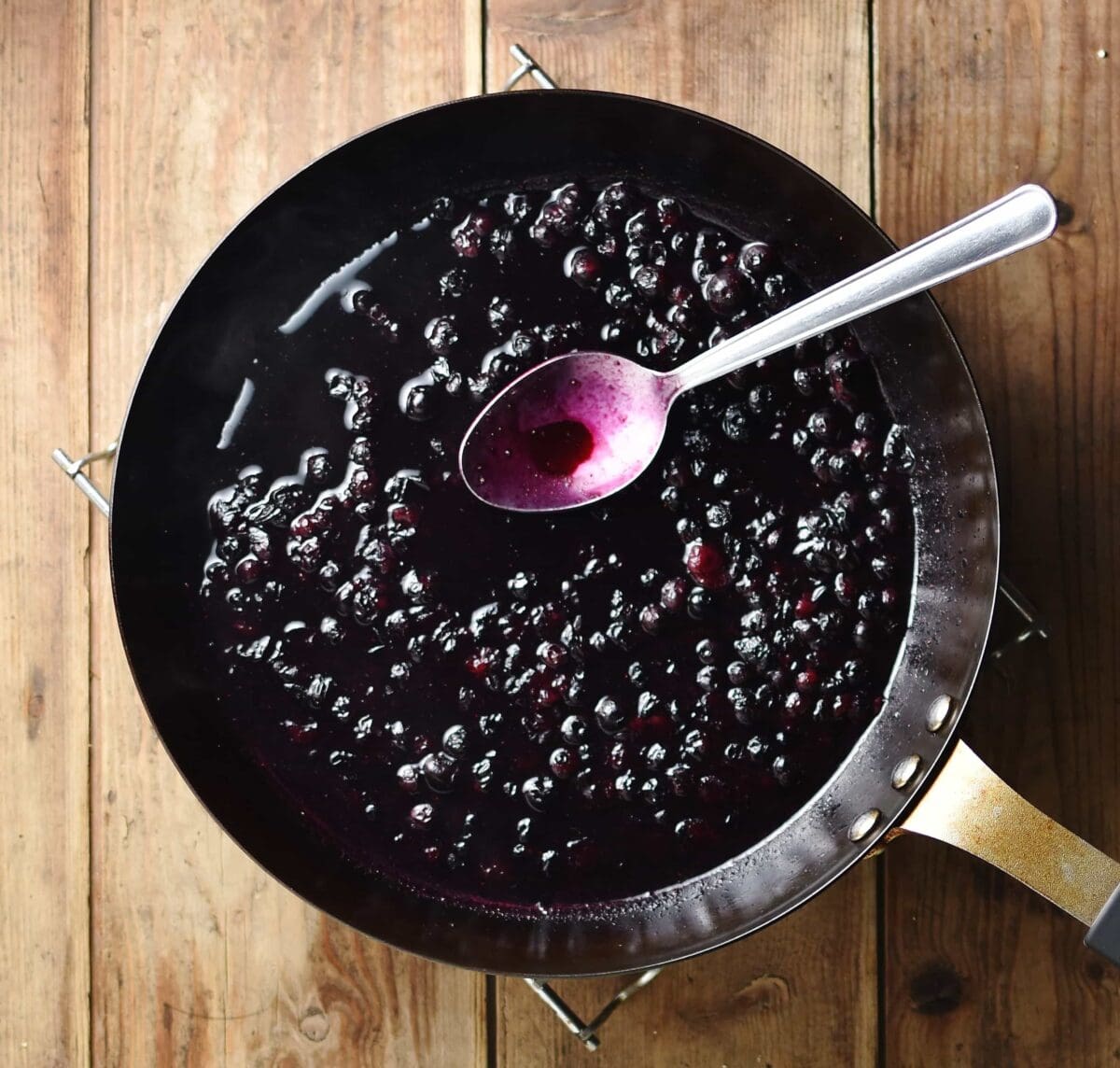 Top down view of blueberry sauce with spoon inside small pan.