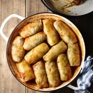 Top down view of cabbage rolls in large white dish with lid in top right corner and blue-and-white cloth in bottom right.