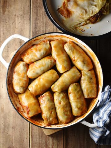 Top down view of cabbage rolls in large white dish with lid in top right corner and blue-and-white cloth in bottom right.