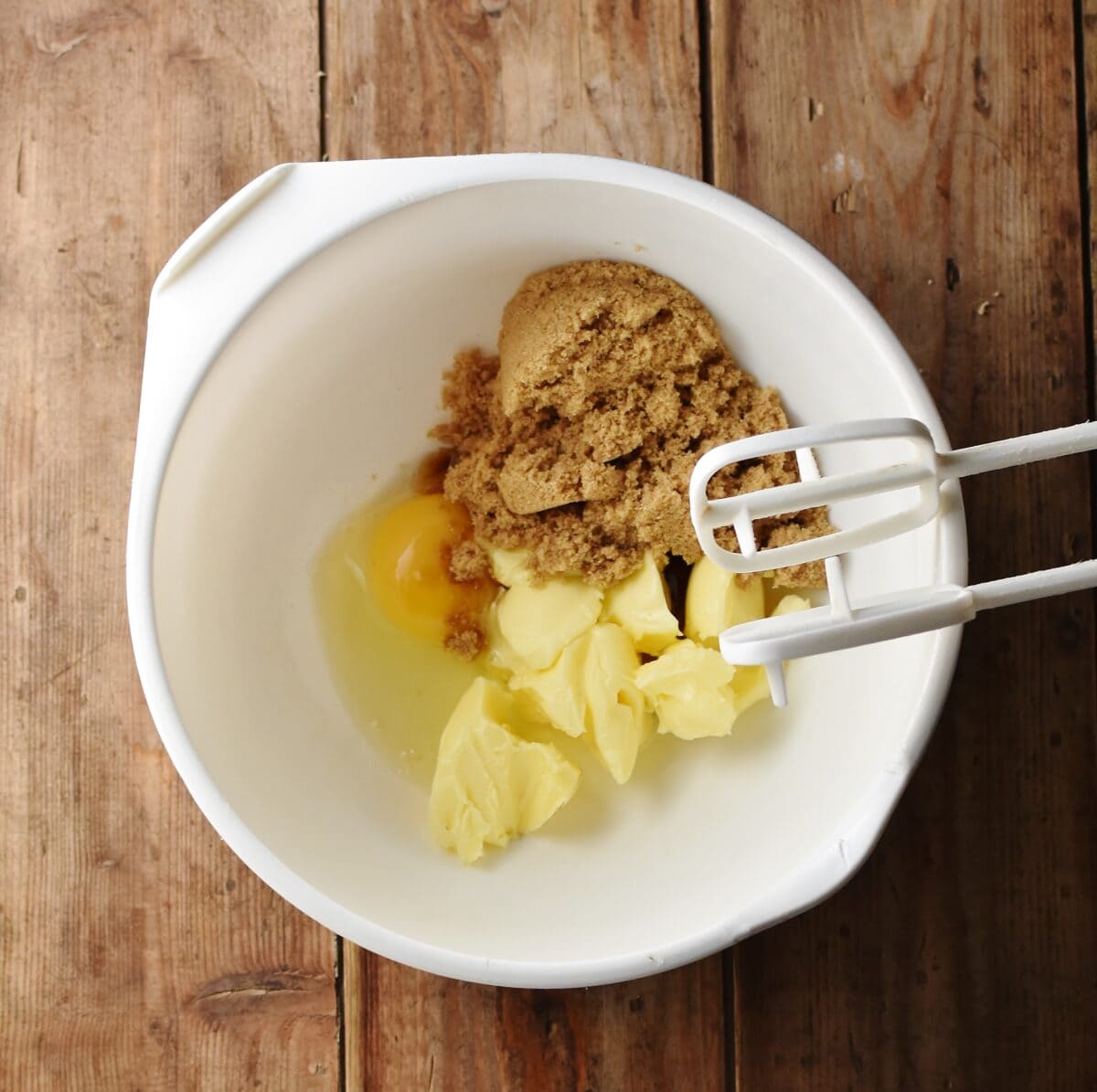 Egg, brown sugar and butter in large white bowl with electric mixer end bits.