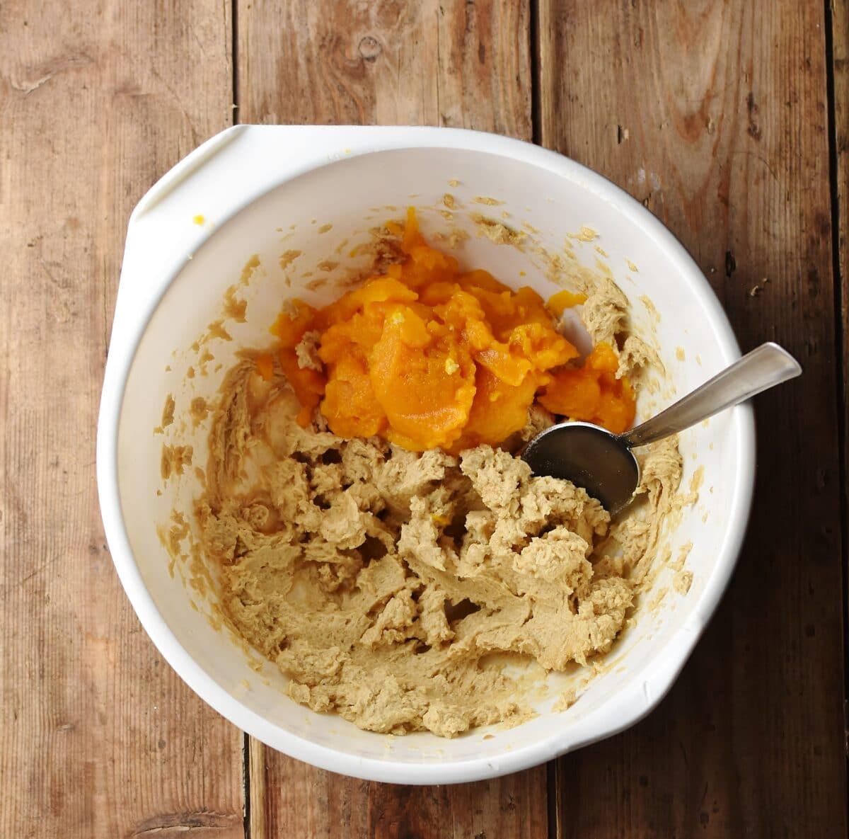 Cookie batter and pumpkin puree with spoon in large white bowl.
