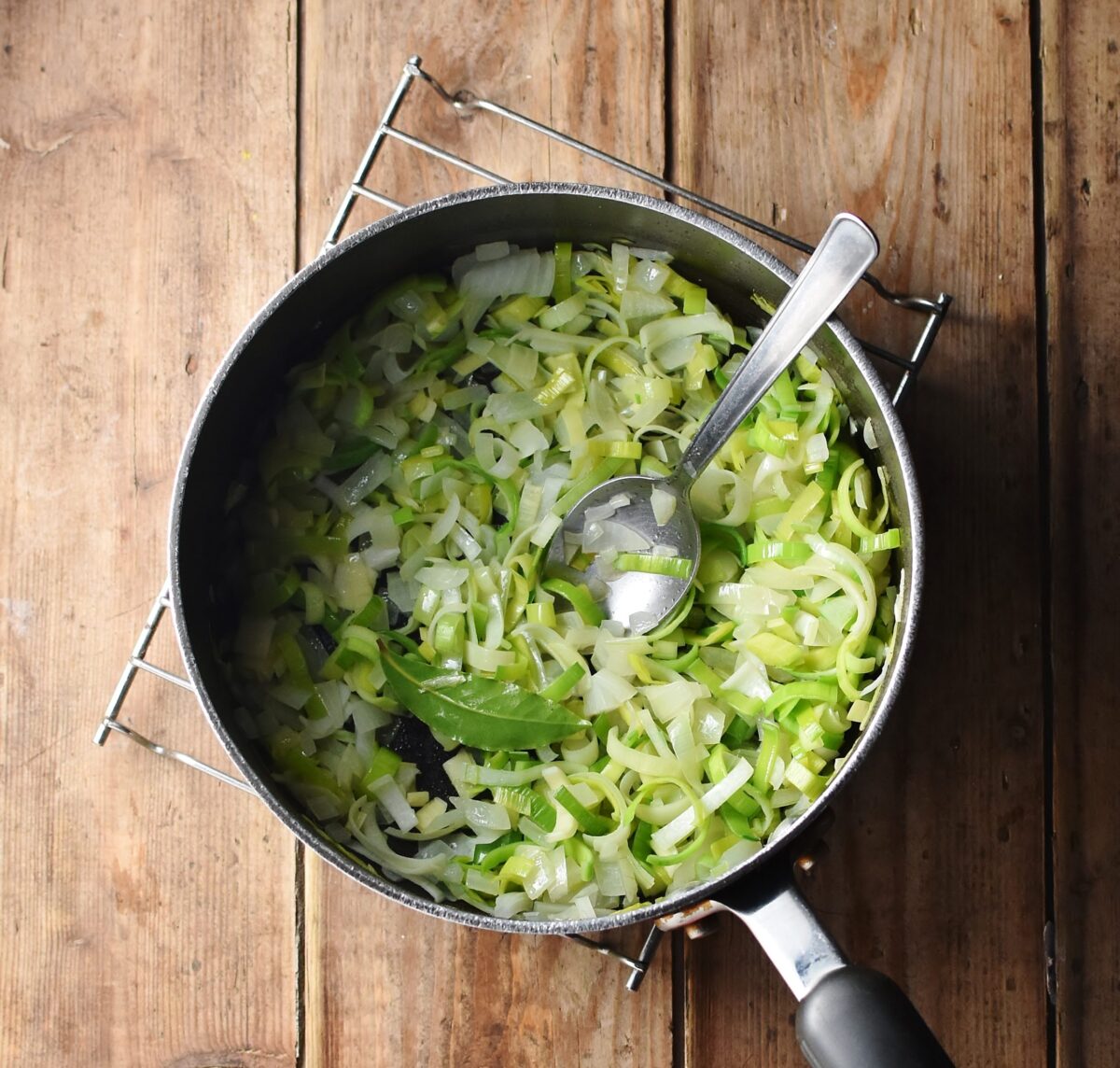 Chopped onion and leek with bay leaf in large pot with spoon.