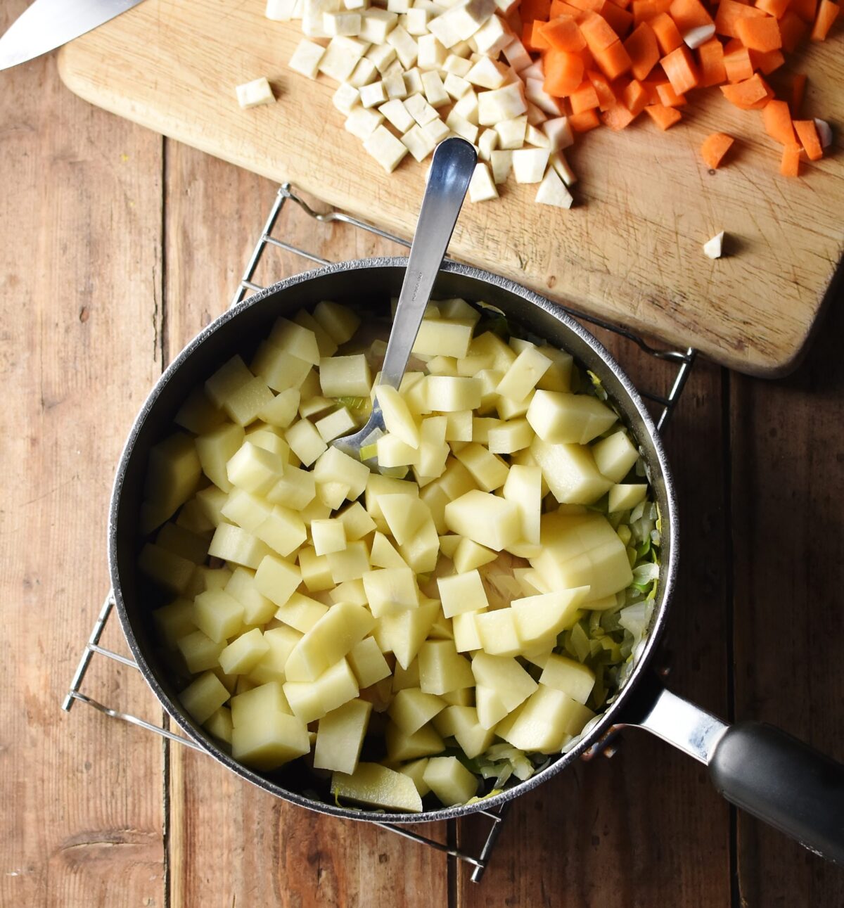 Cubed potatoes in large pot with spoon, and cubed vegetables in background.