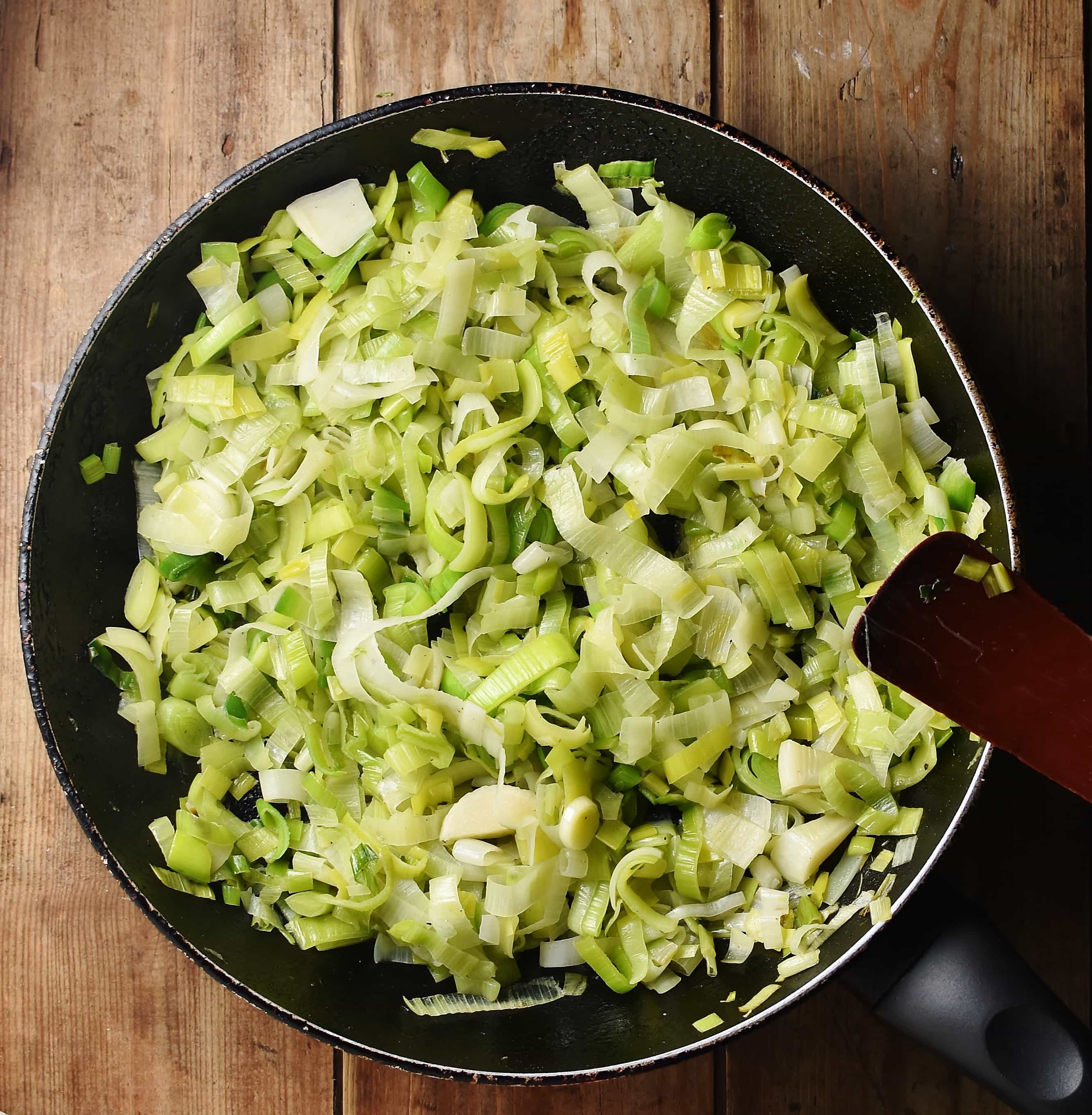 Chopped leeks in large skillet with black spatula to the right.