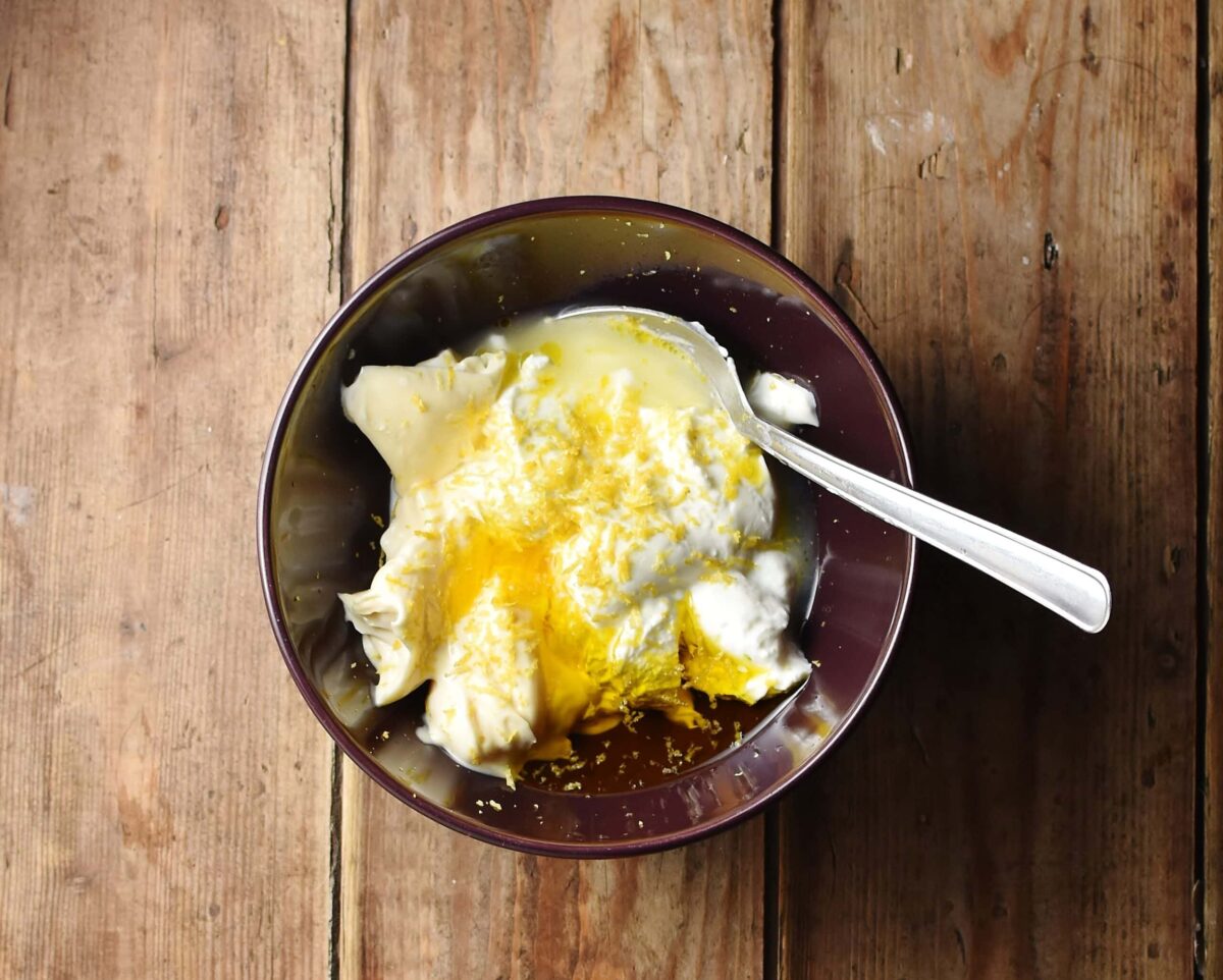 Yogurt, lemon juice and zest, oil and spoon in purple bowl.