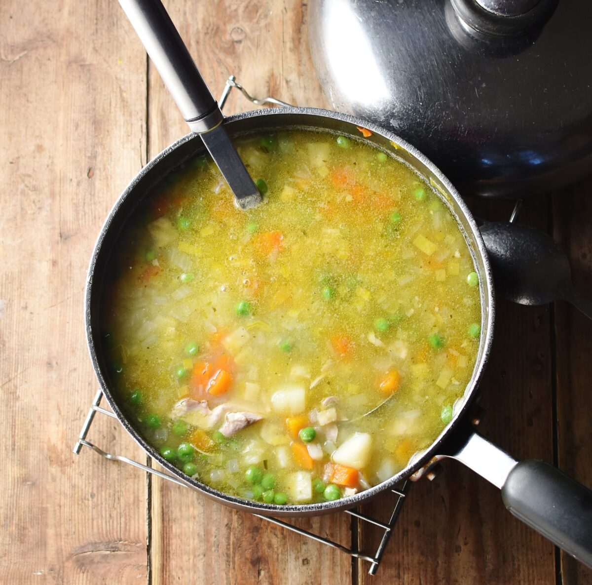 Chunky chicken potato soup in large pot with ladle and lid in top right.