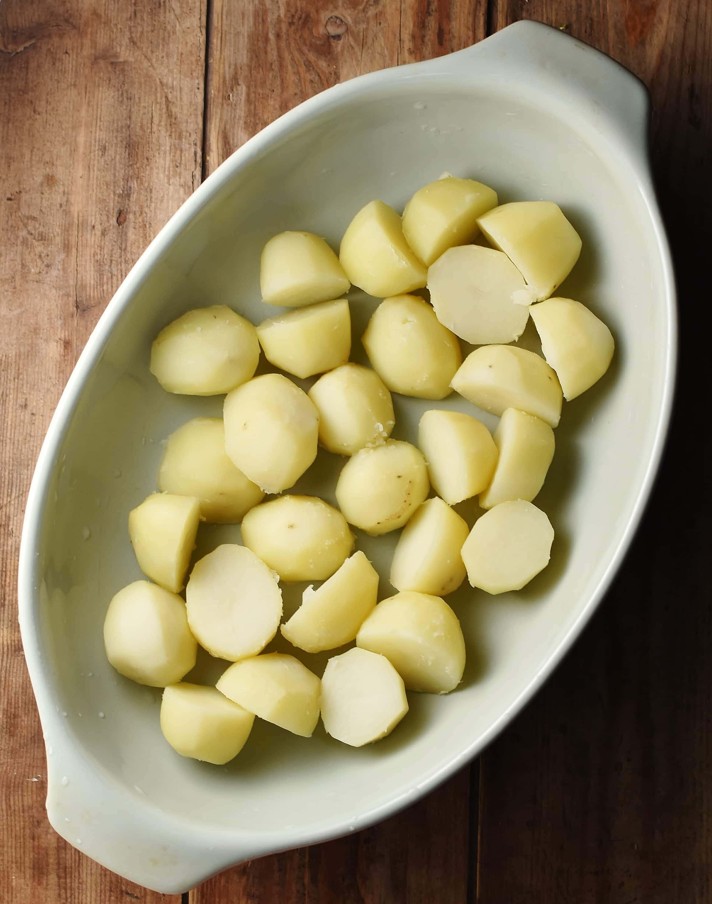 Peeled, halved potatoes in oval casserole dish.