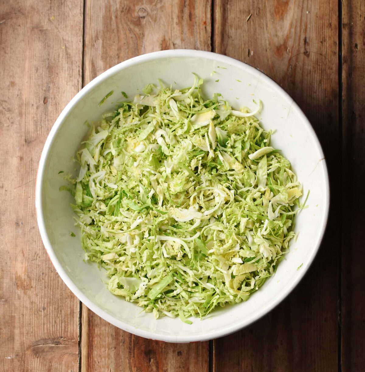 Top down view of shredded brussel sprouts in large white bowl.