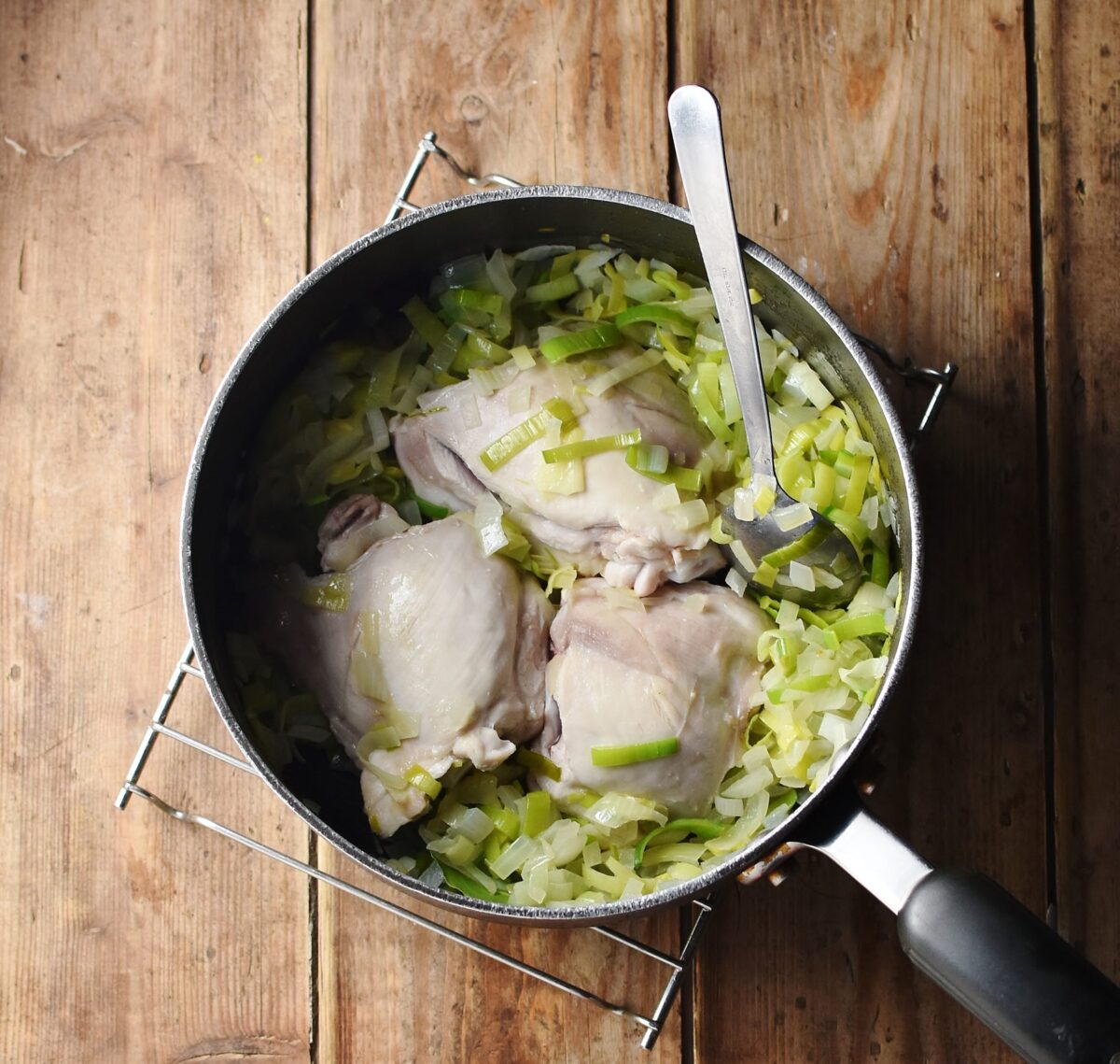 Chopped onion and leek and 3 skinless chicken thighs in large pot with spoon.
