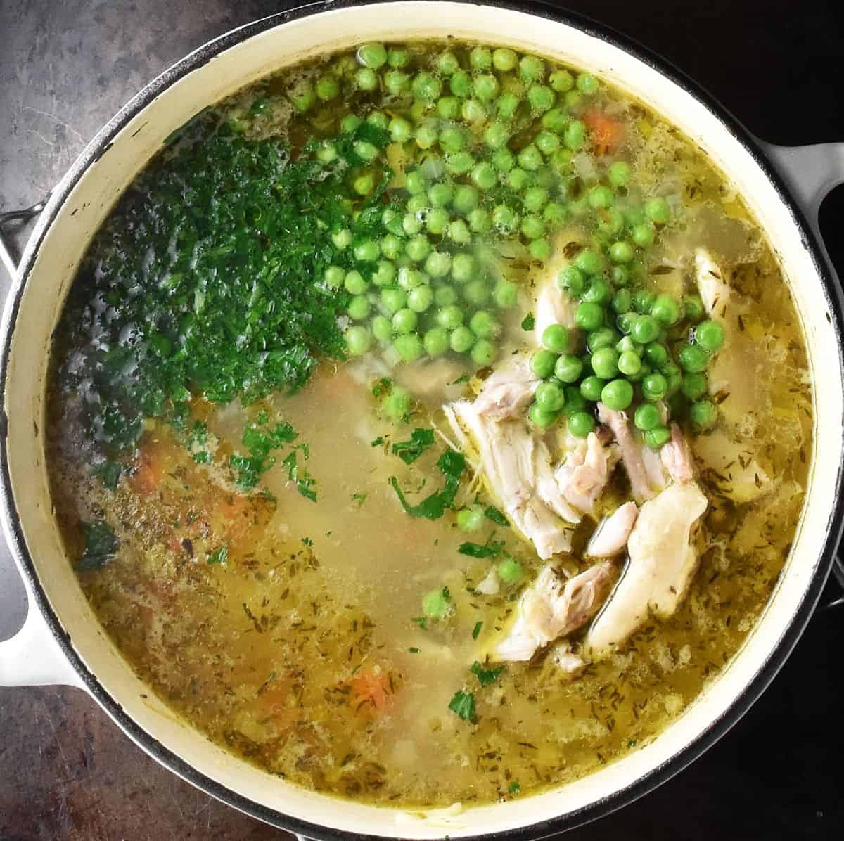 Soup with chicken pieces, chopped herbs and peas in white pot.