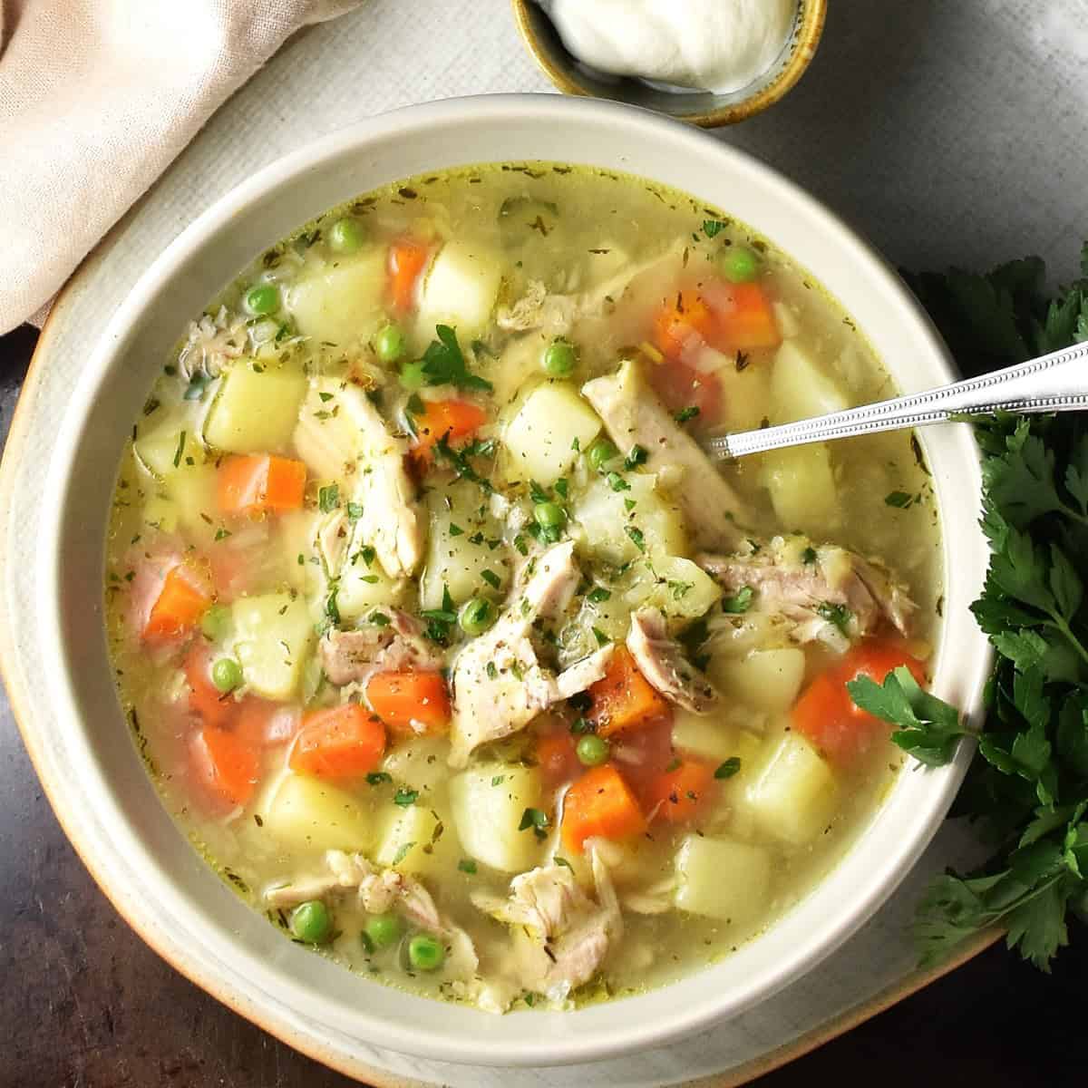 Top down view of chicken and potato soup with carrots in white bowl with spoon.